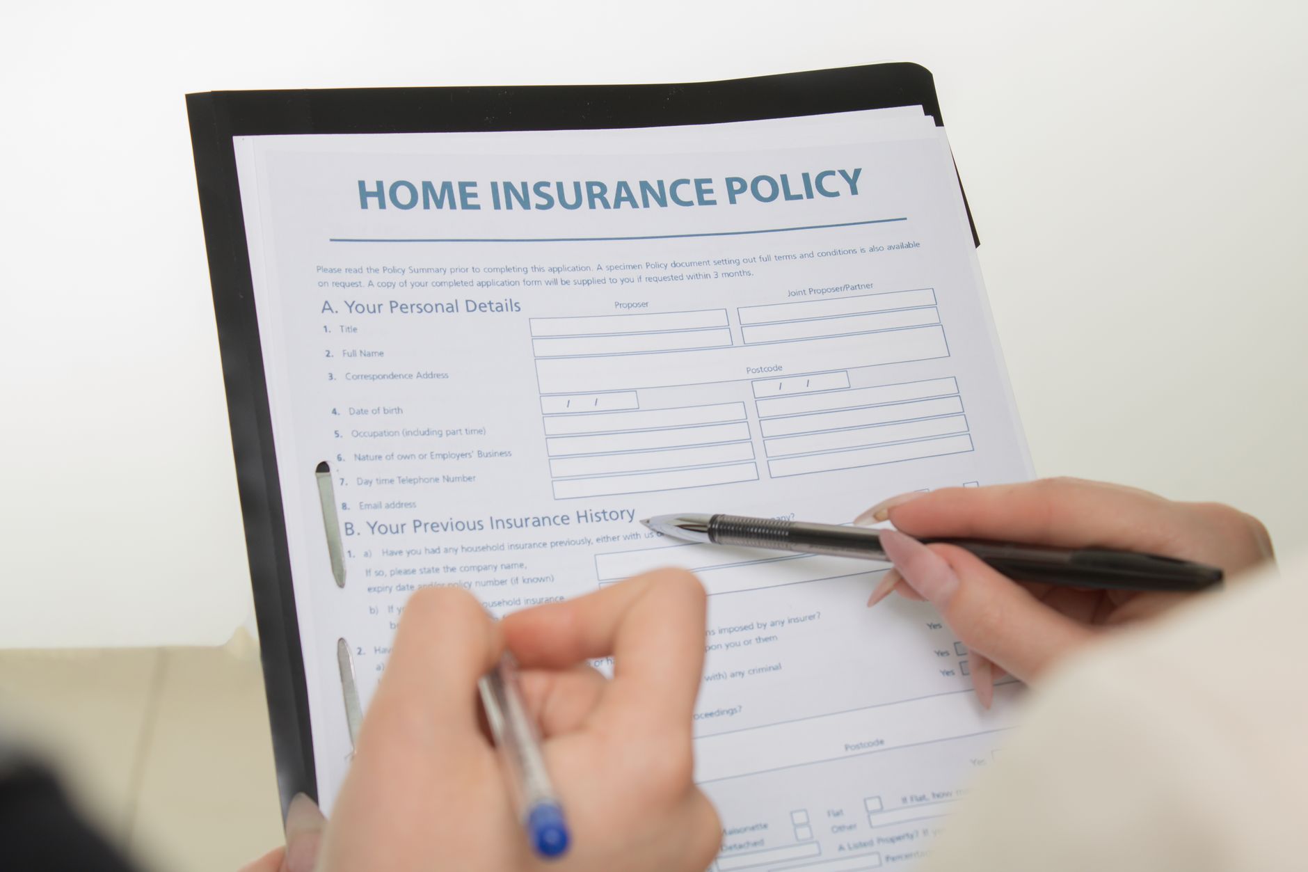 Hands holding pens filling out a home insurance policy document for coverage