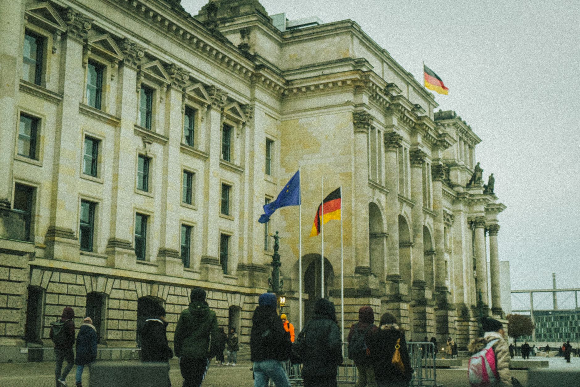 People walking outside a historic building in Germany with flags flying on