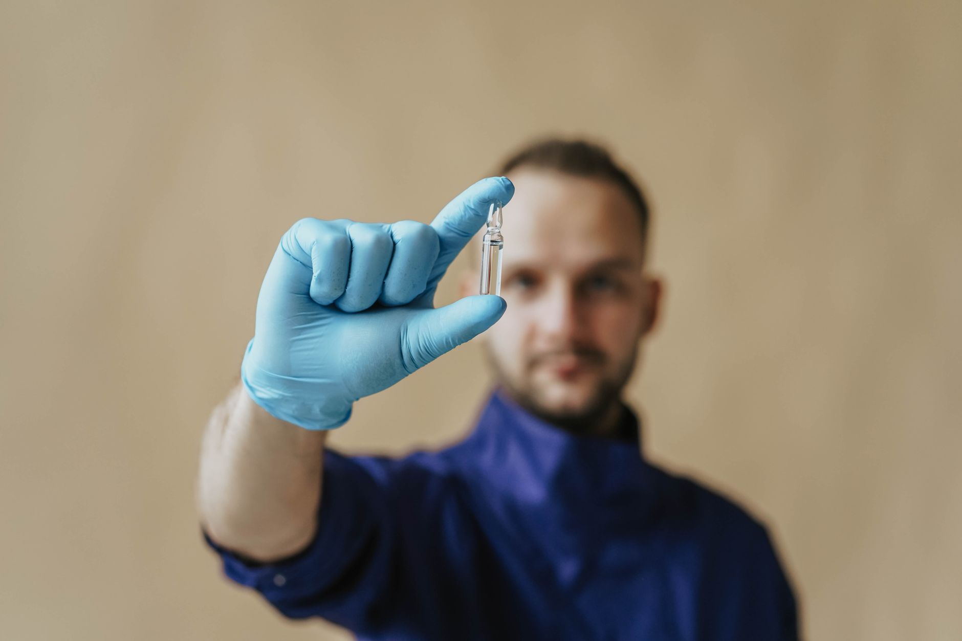A male healthcare worker in protective gloves holding a small vial, focusing