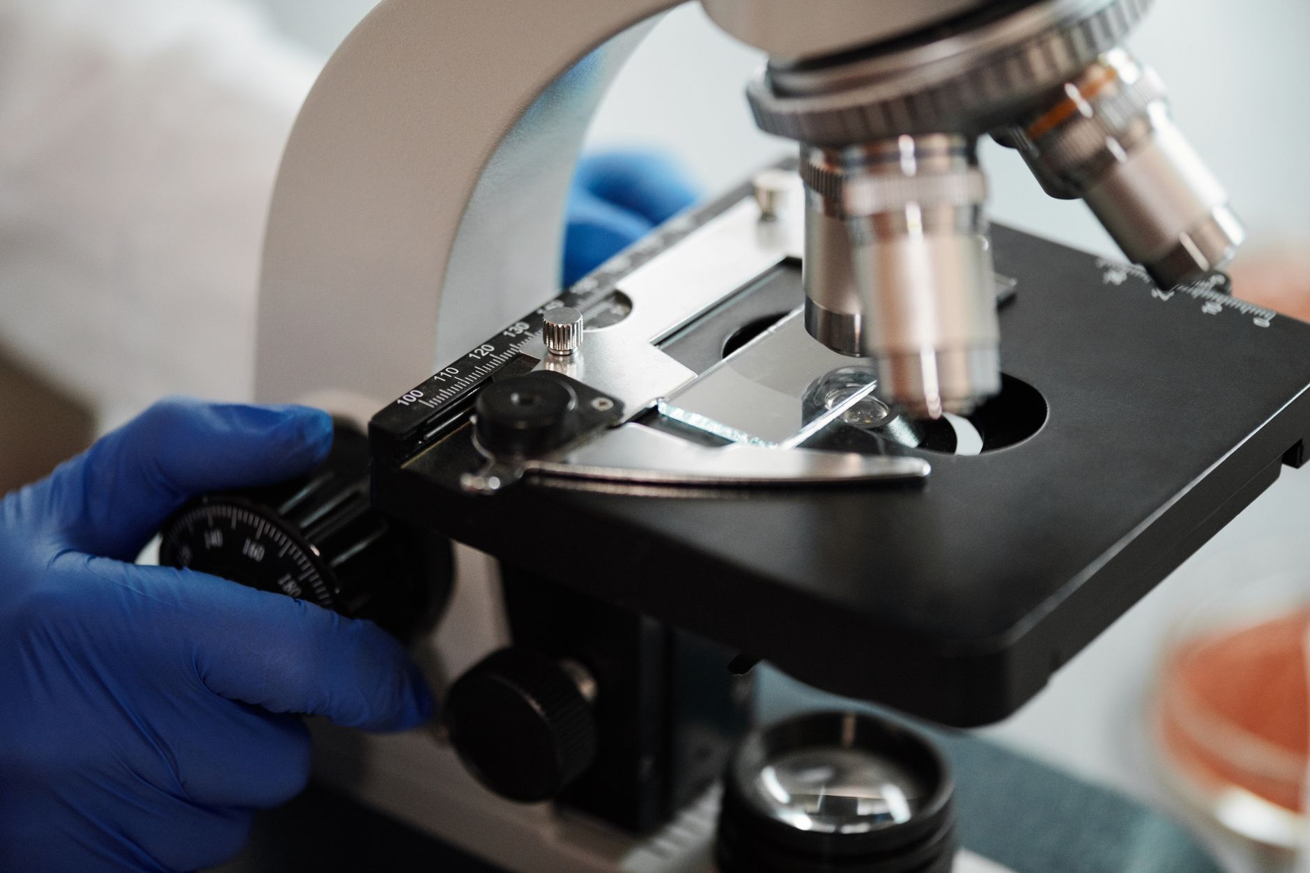 Close-up image of a scientist's gloved hand adjusting a microscope in a