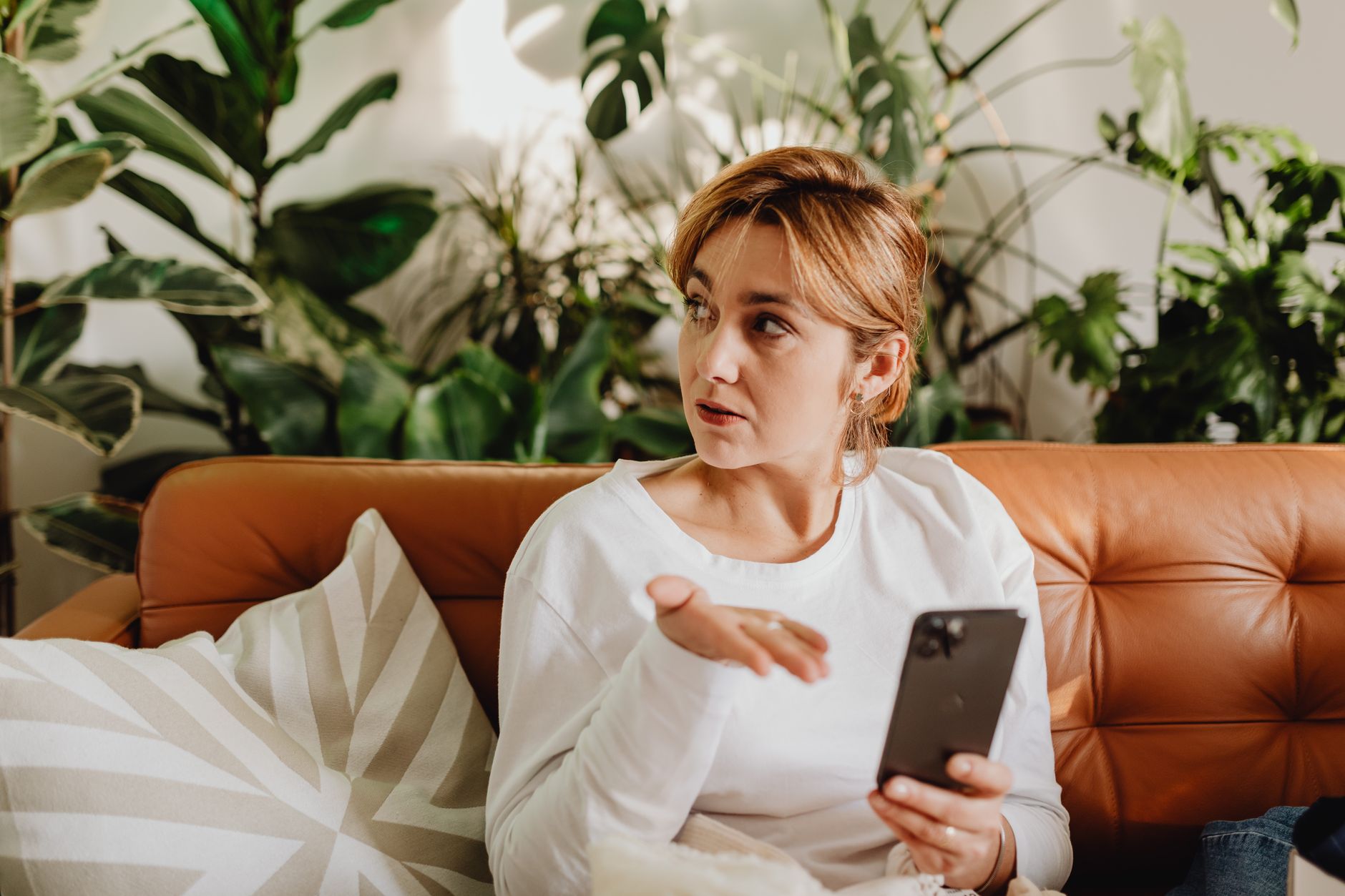 A woman sits on a sofa, interacting with her smartphone in a