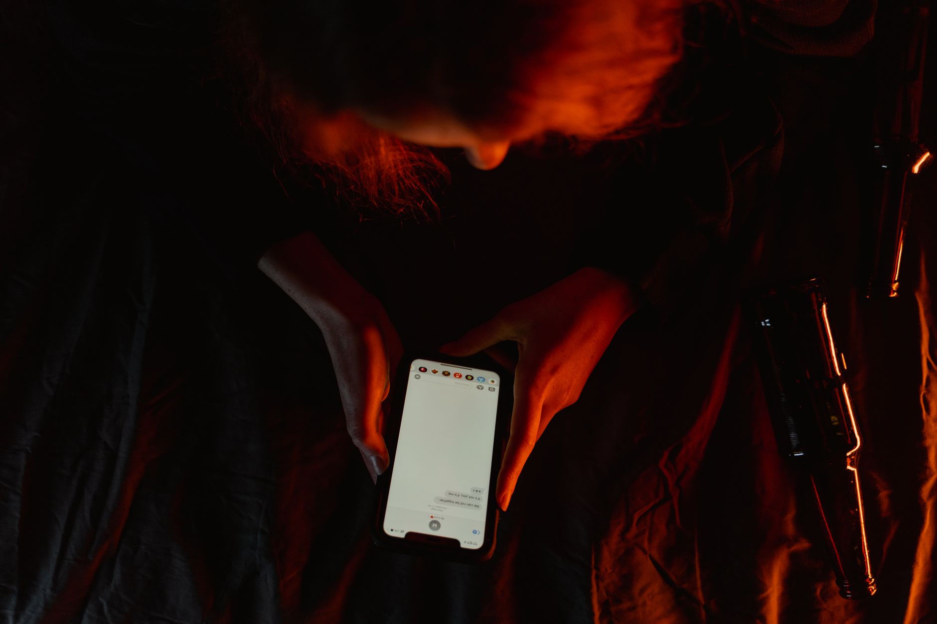 A person using a smartphone in dim, moody lighting with a dark background.