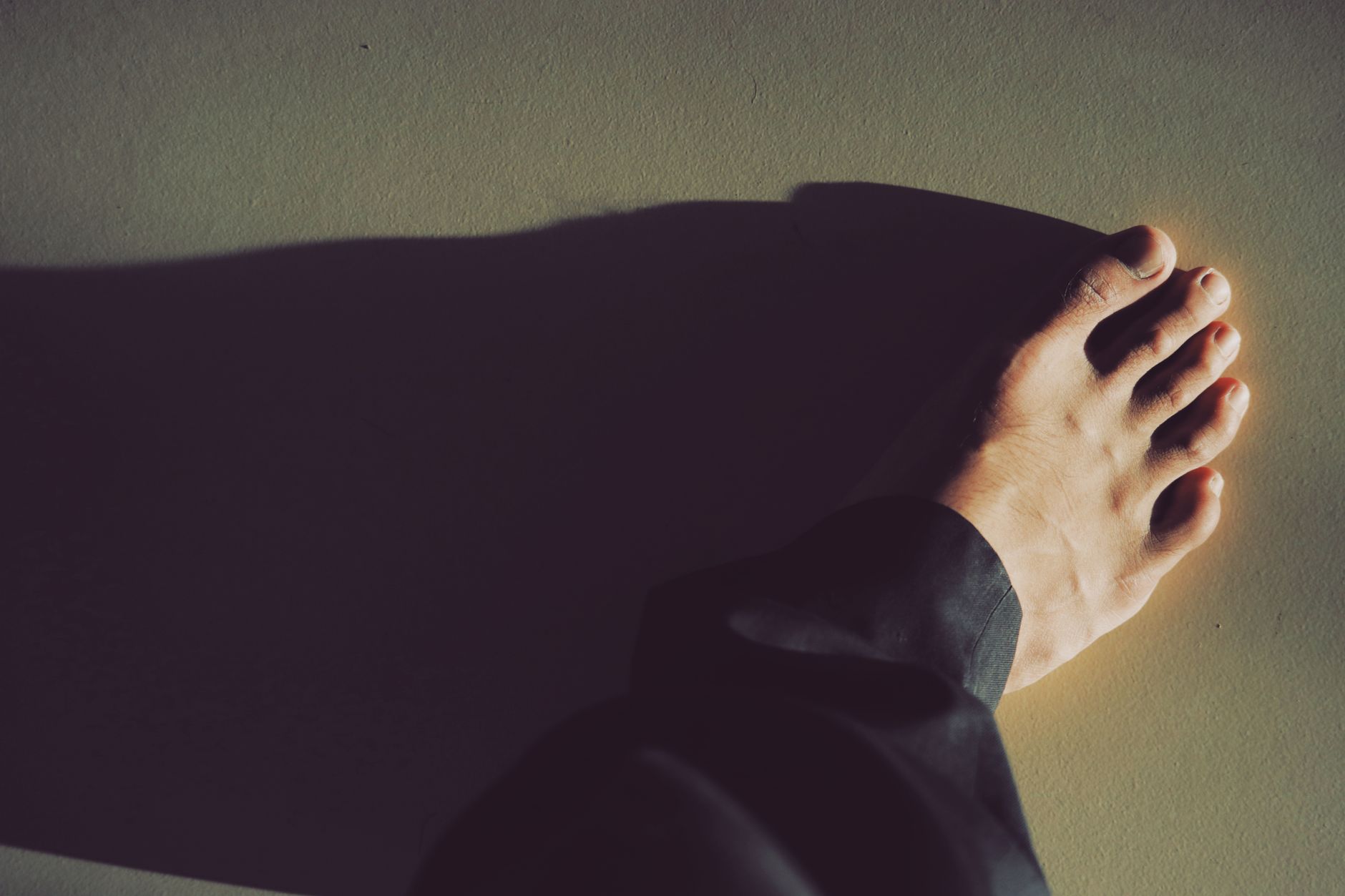 A close-up photo capturing a bare foot casting a dramatic shadow on