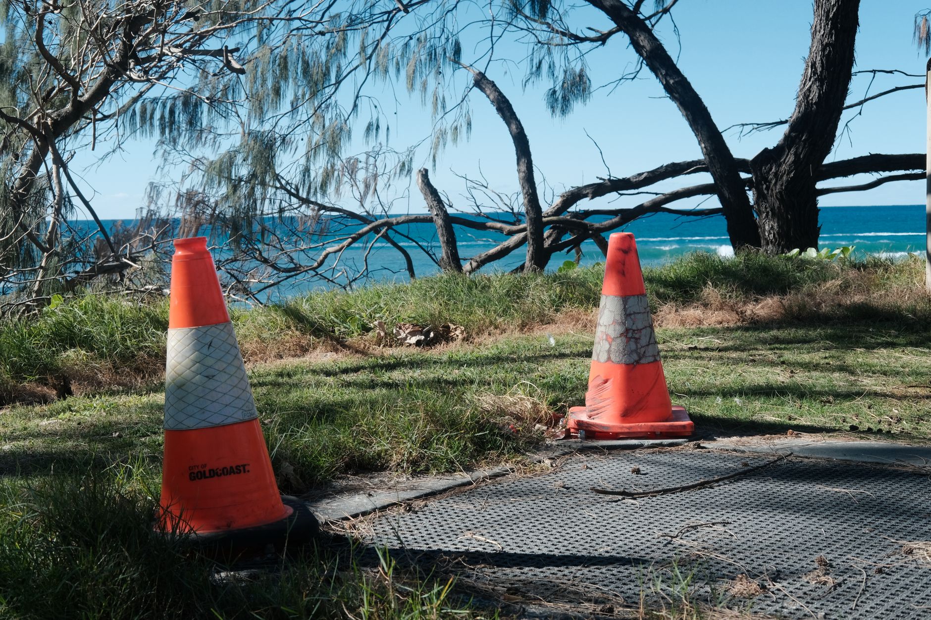 Orange traffic cones placed on a grass path by the sea under