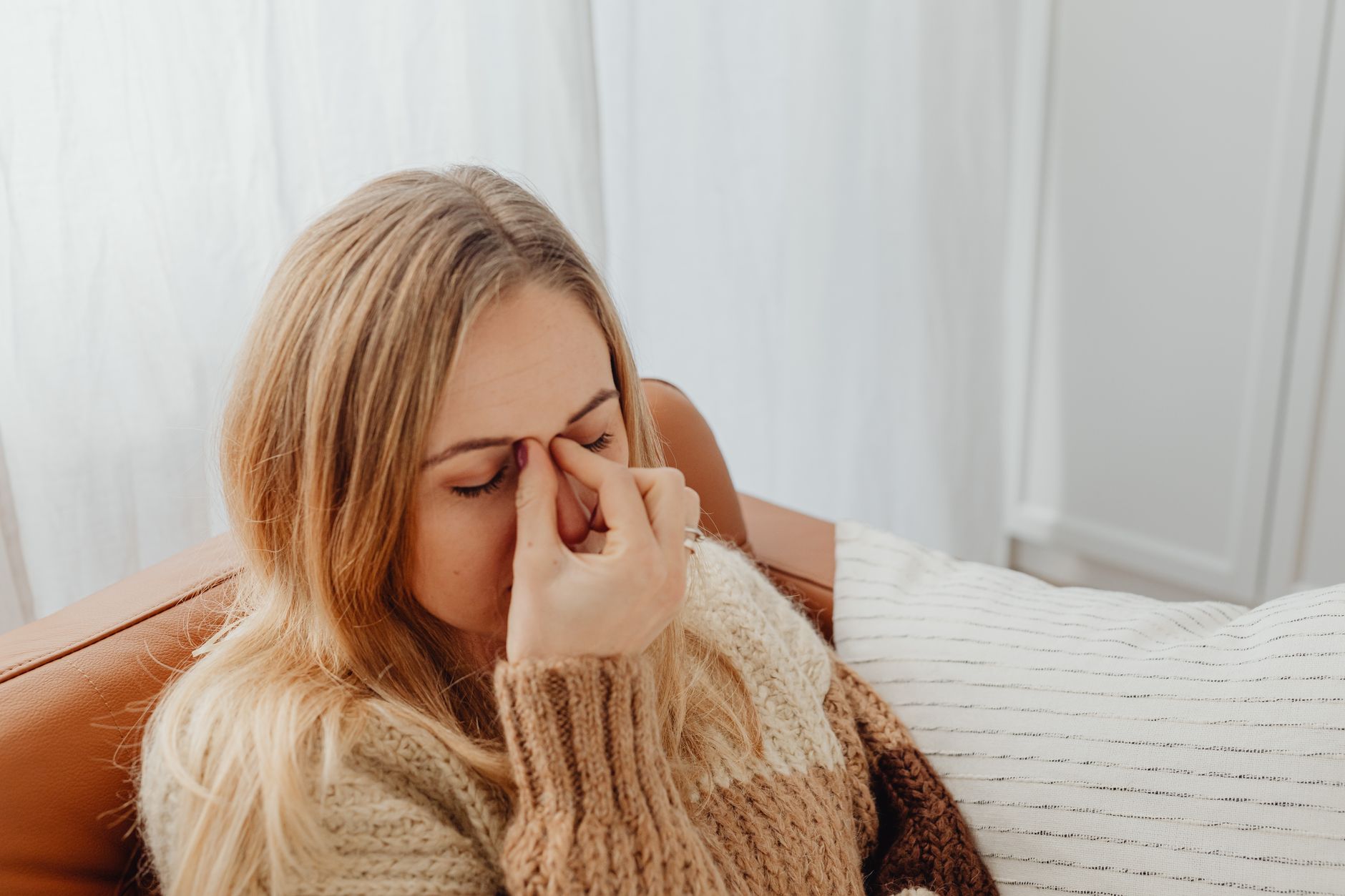 A woman sitting on a couch with eyes closed, holding her nose