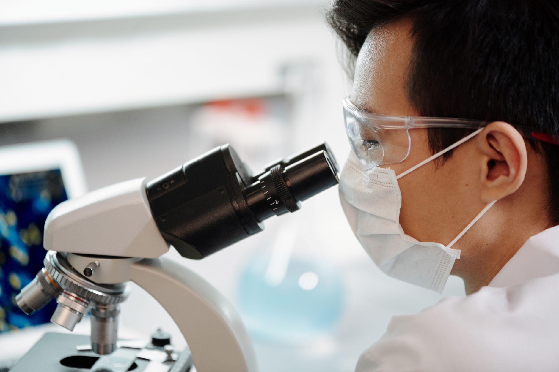 Scientist wearing face mask and goggles examining samples through a microscope in