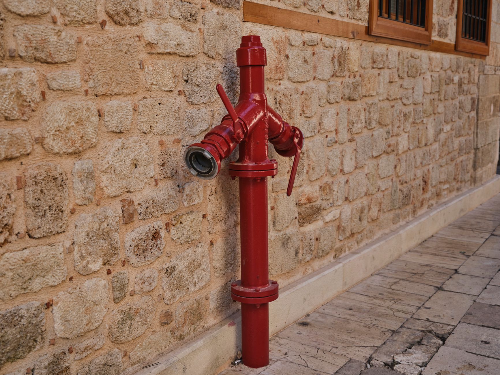 Close-up of a red fire hydrant mounted on a cobblestone wall on a street.