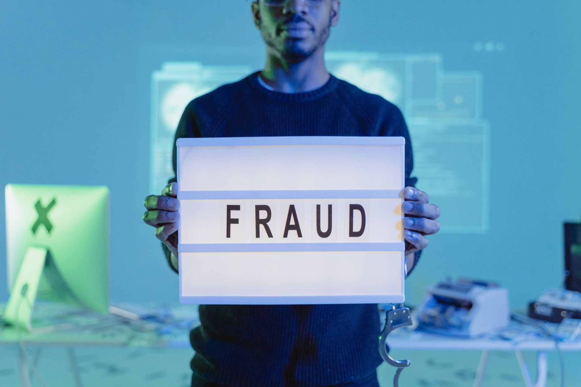 A man holding a sign reading 'FRAUD' in a tech environment, highlighting