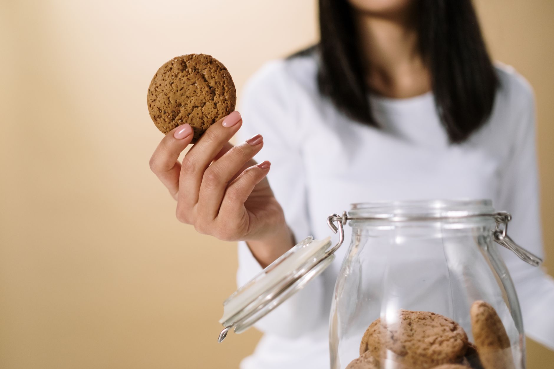 Close-up of a woman's hand holding a cookie from a glass jar,