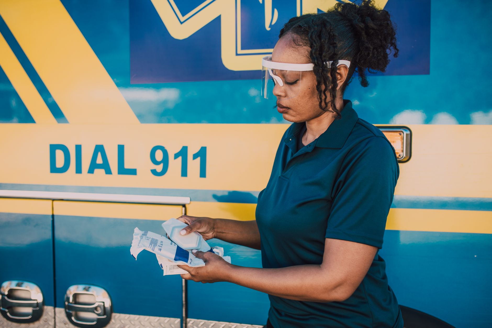 Female paramedic organizing medical supplies beside an emergency ambulance.