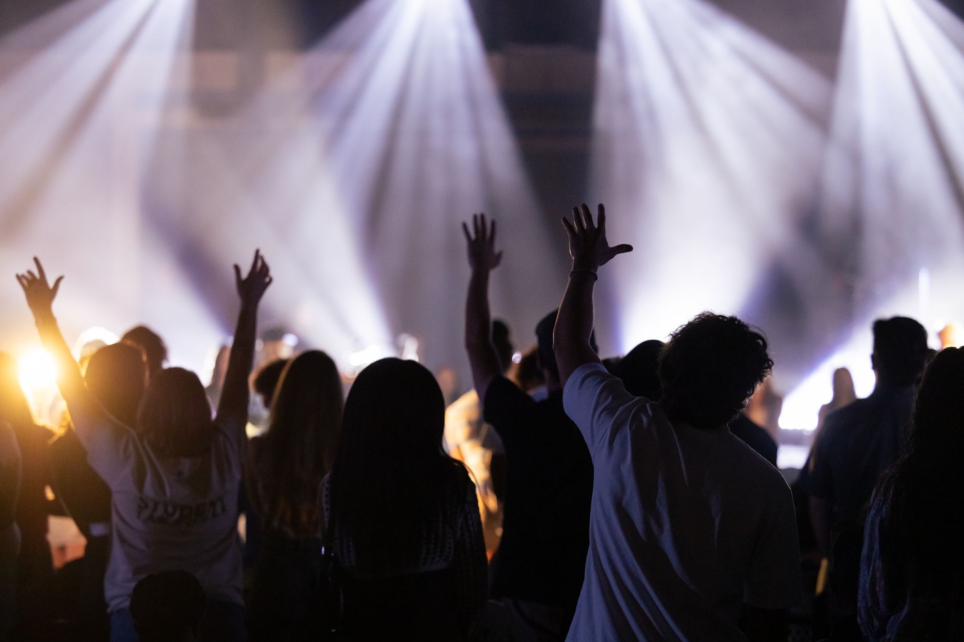 Silhouette of a crowd with raised hands enjoying a worship concert with