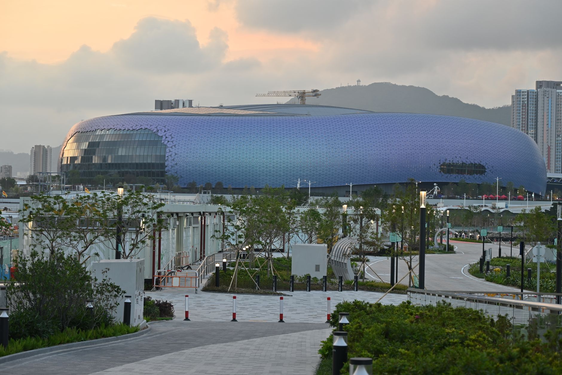 Panoramic view of a futuristic stadium surrounded by greenery, captured at dusk.