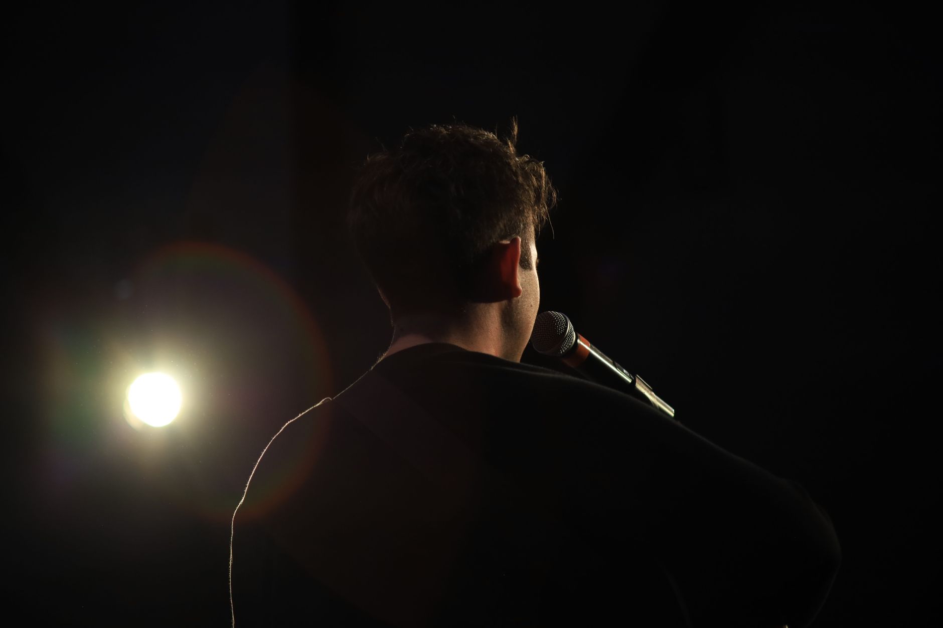 Silhouette of a singer on stage with a microphone, spotlight in the black background.