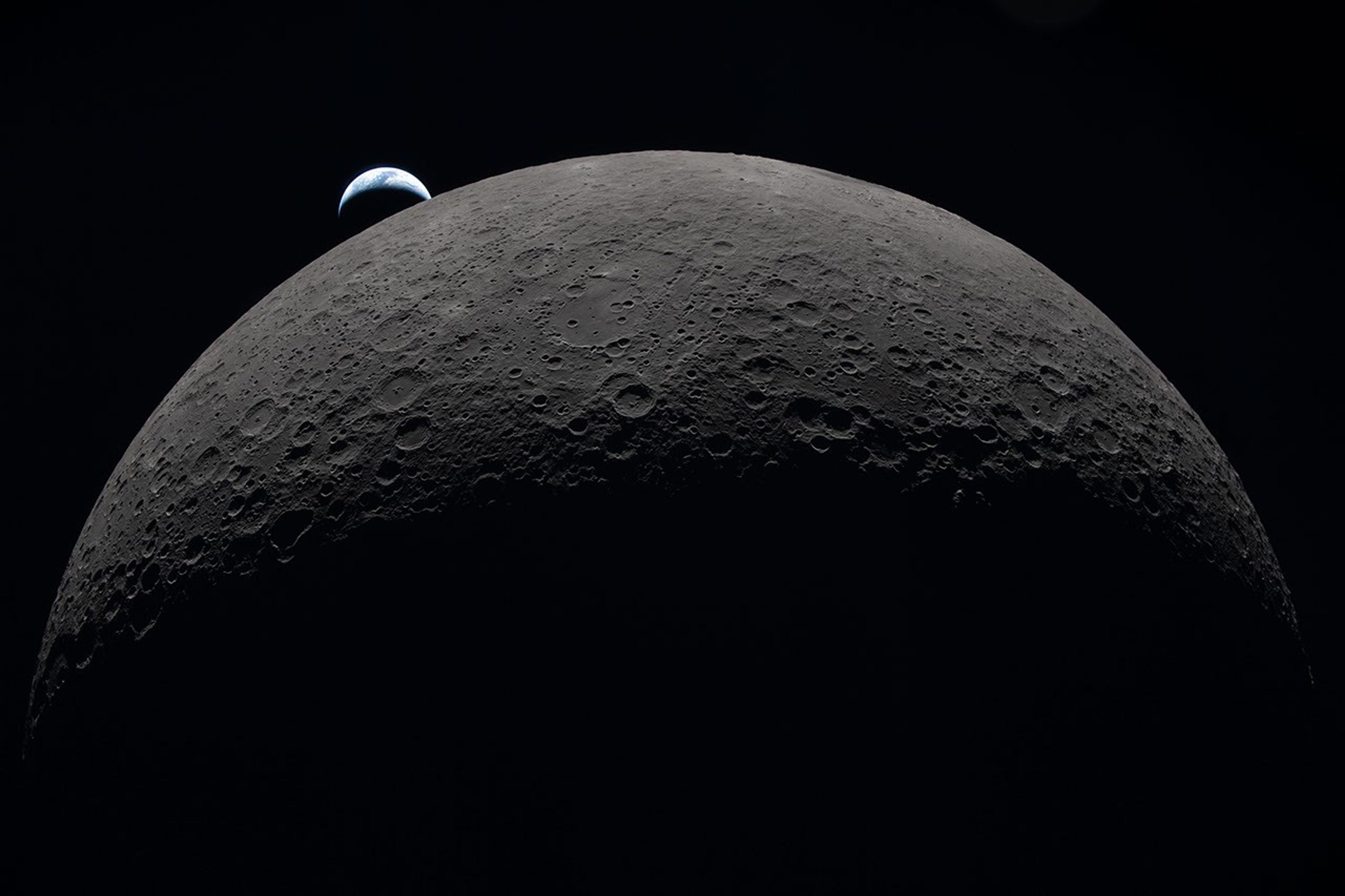 The gray-brown, heavily cratered Moon dominates the frame against black space, with