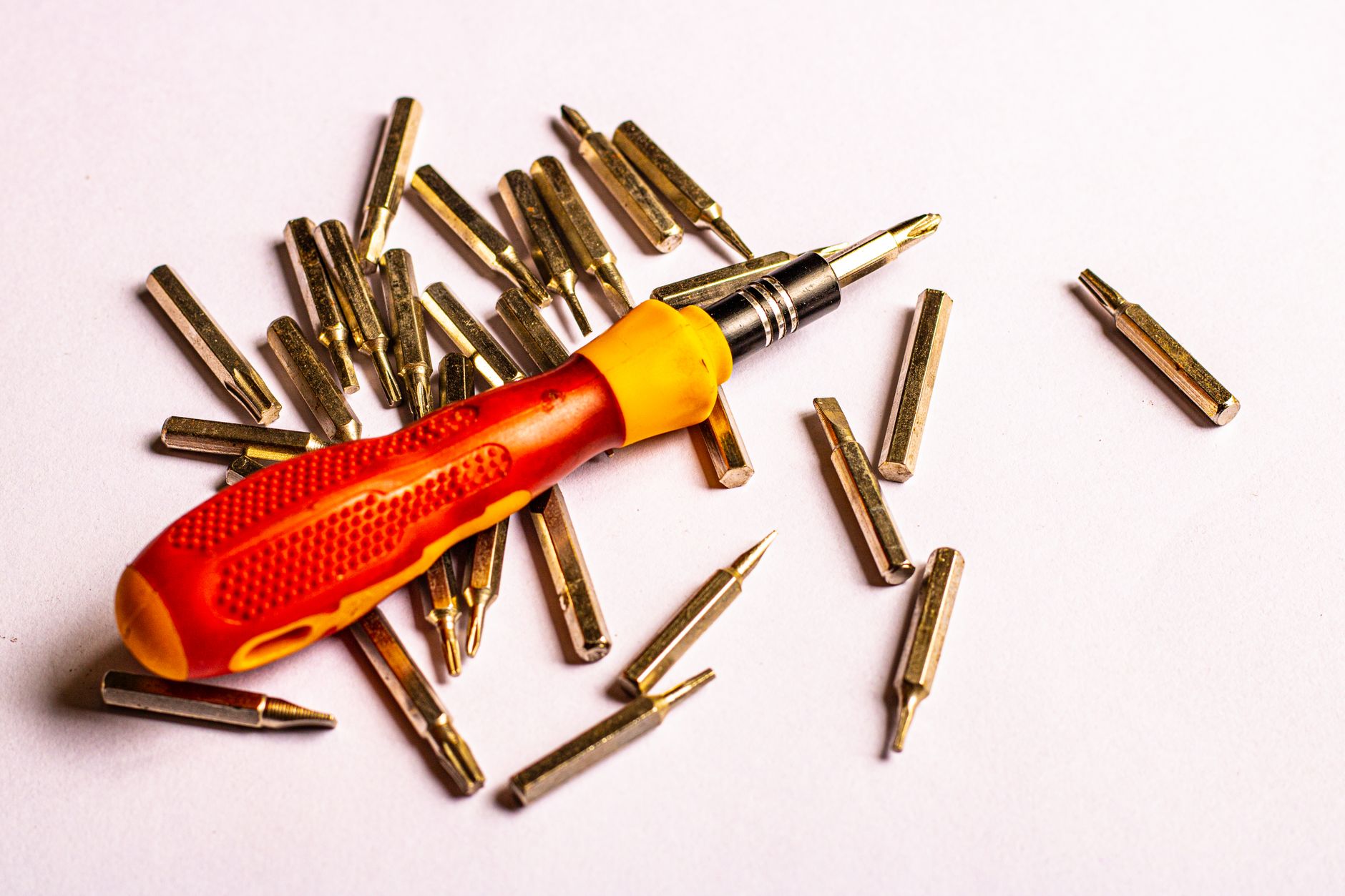 A close-up of a screwdriver with various metal bits on a white
