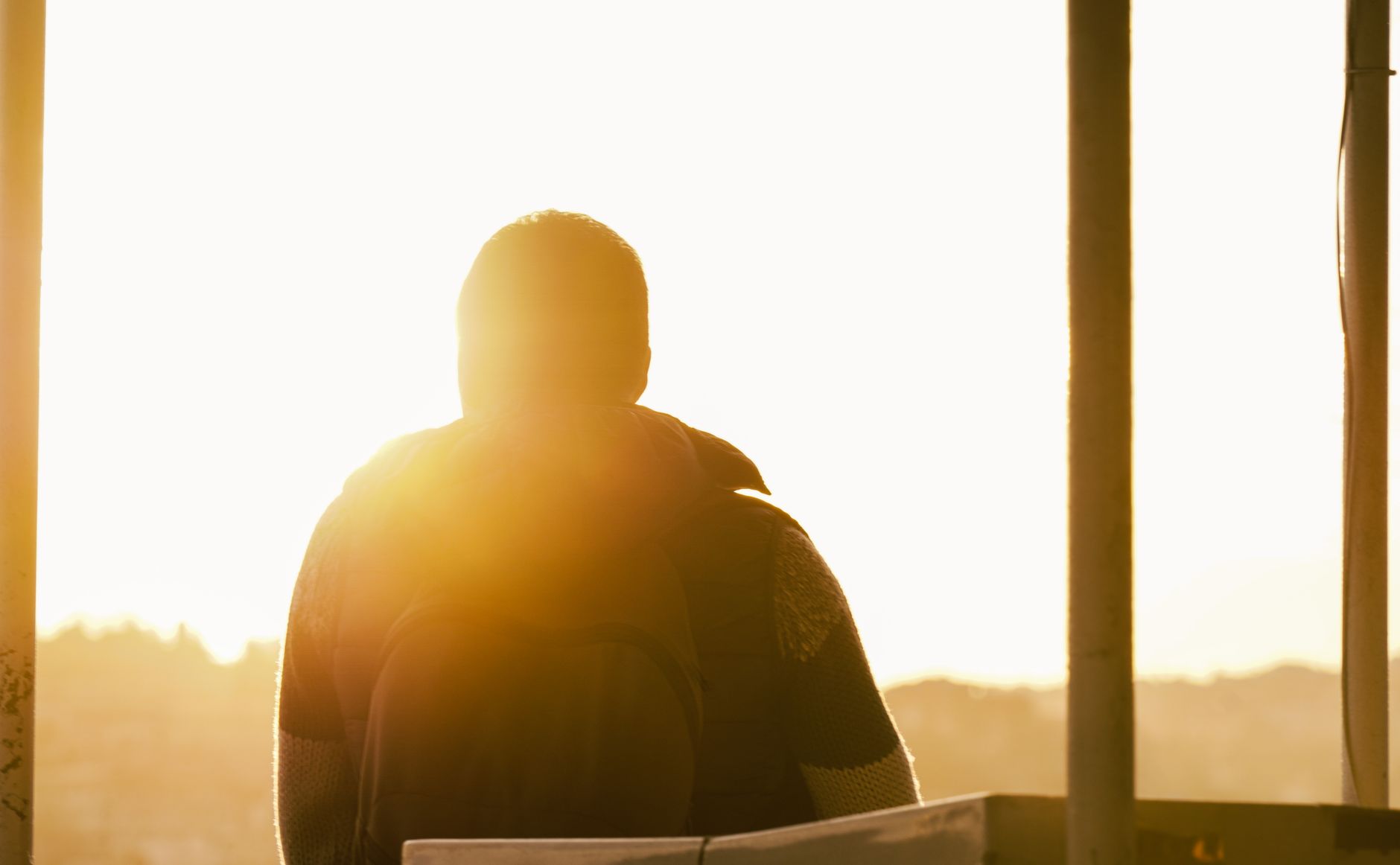 A person stands backlit by the sun, looking at a scenic sunset