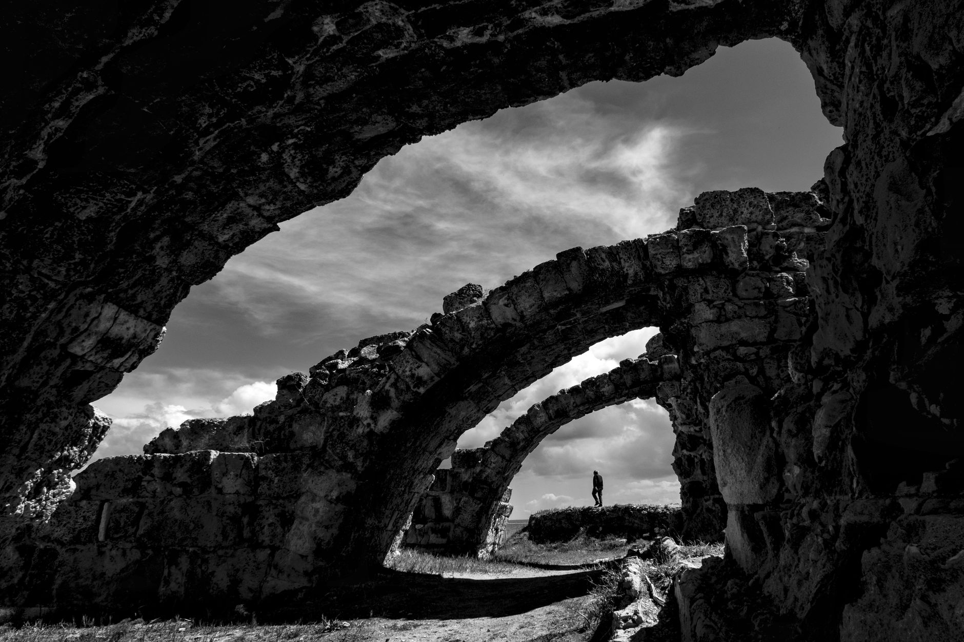 Black and white image showcasing a silhouette under ancient stone arches against