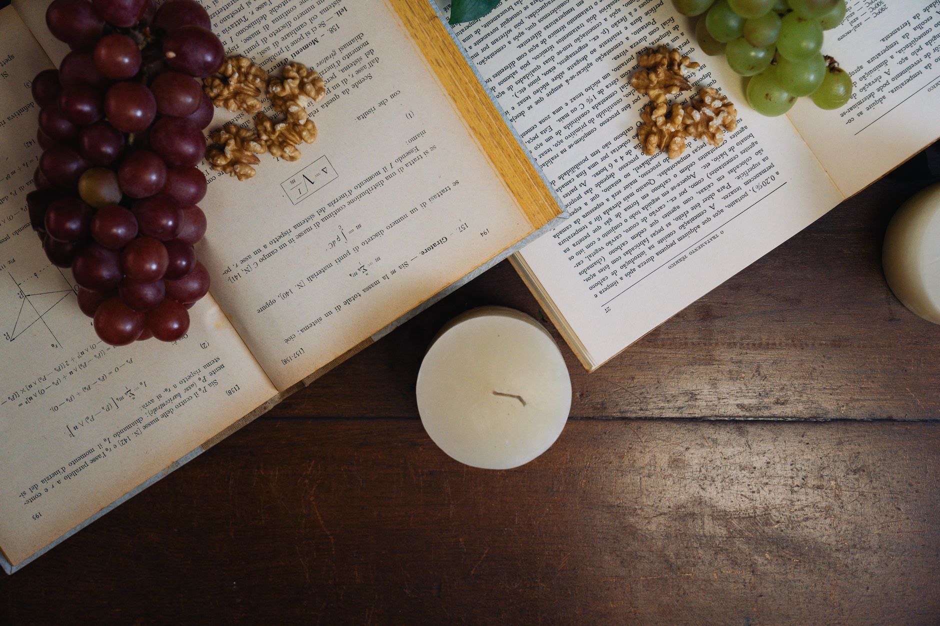 Aesthetic still life with grapes, walnuts, and open books by candlelight on