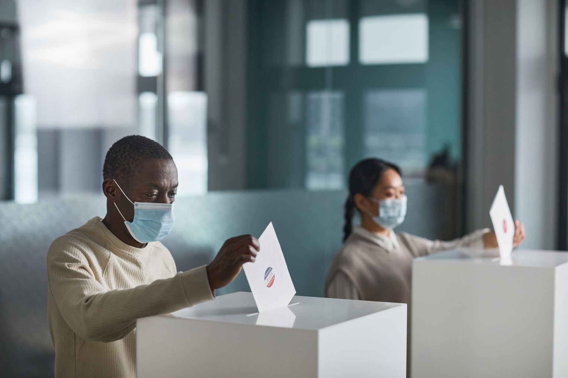 People wearing face masks cast ballots in a public indoor polling station