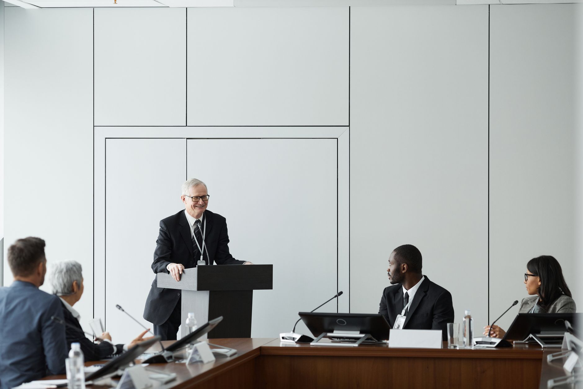 Formal business meeting with a diverse group and speaker at a podium in a conference room.