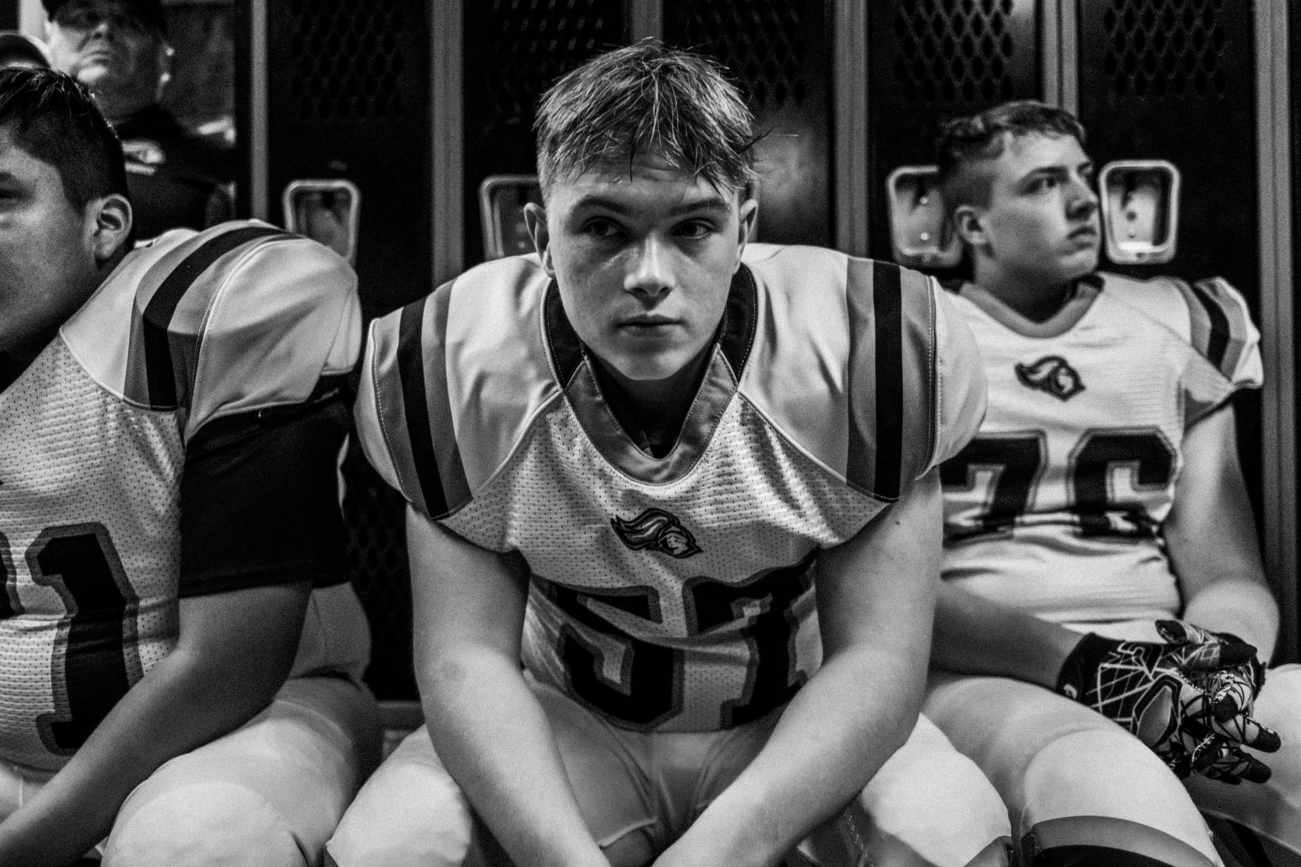 Teen football players prepare for game in the locker room, showcasing focus and teamwork.
