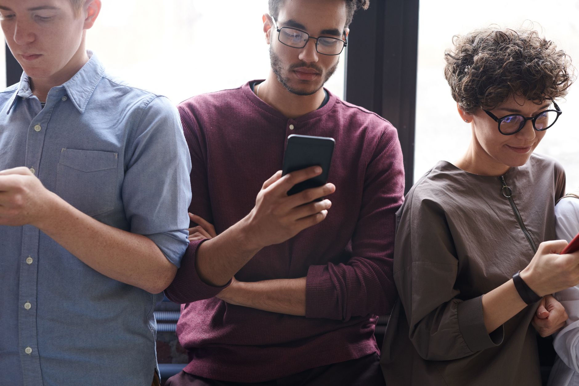 A diverse group of people actively using smartphones indoors. Modern technology and
