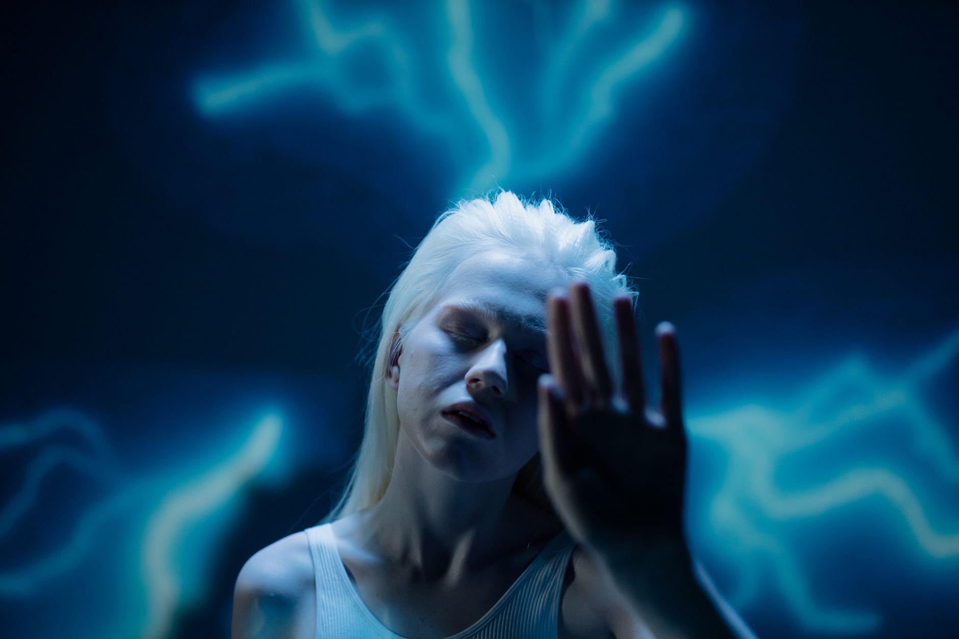 A dramatic studio portrait of a woman with eyes closed, posing against a glowing blue abstract background.