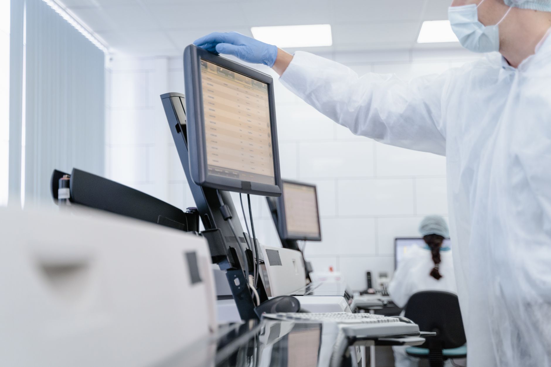 Researcher in PPE reviews data on a digital screen in a modern