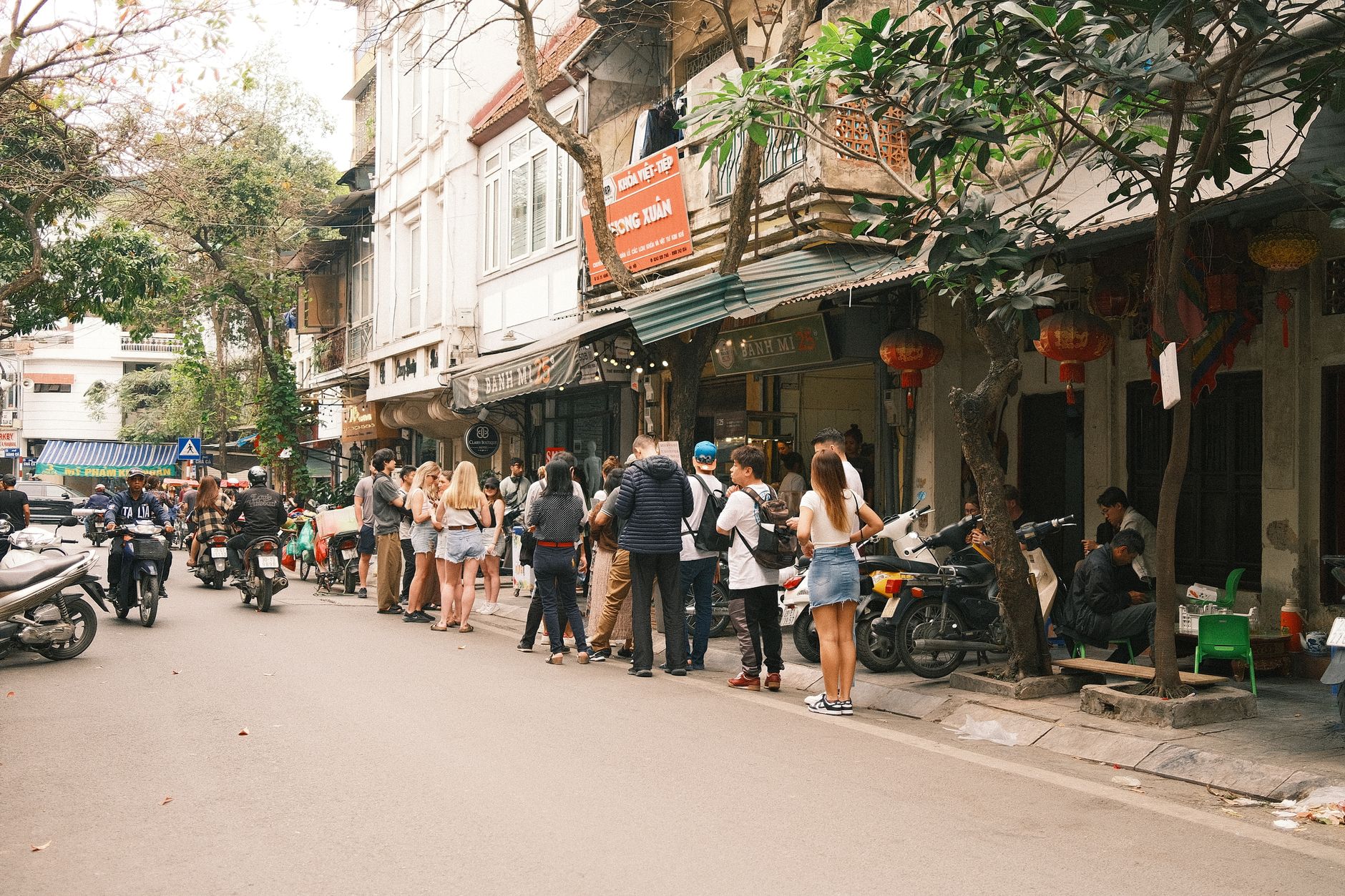 Bustling street scene in Hanoi featuring people lined up outside a shop,