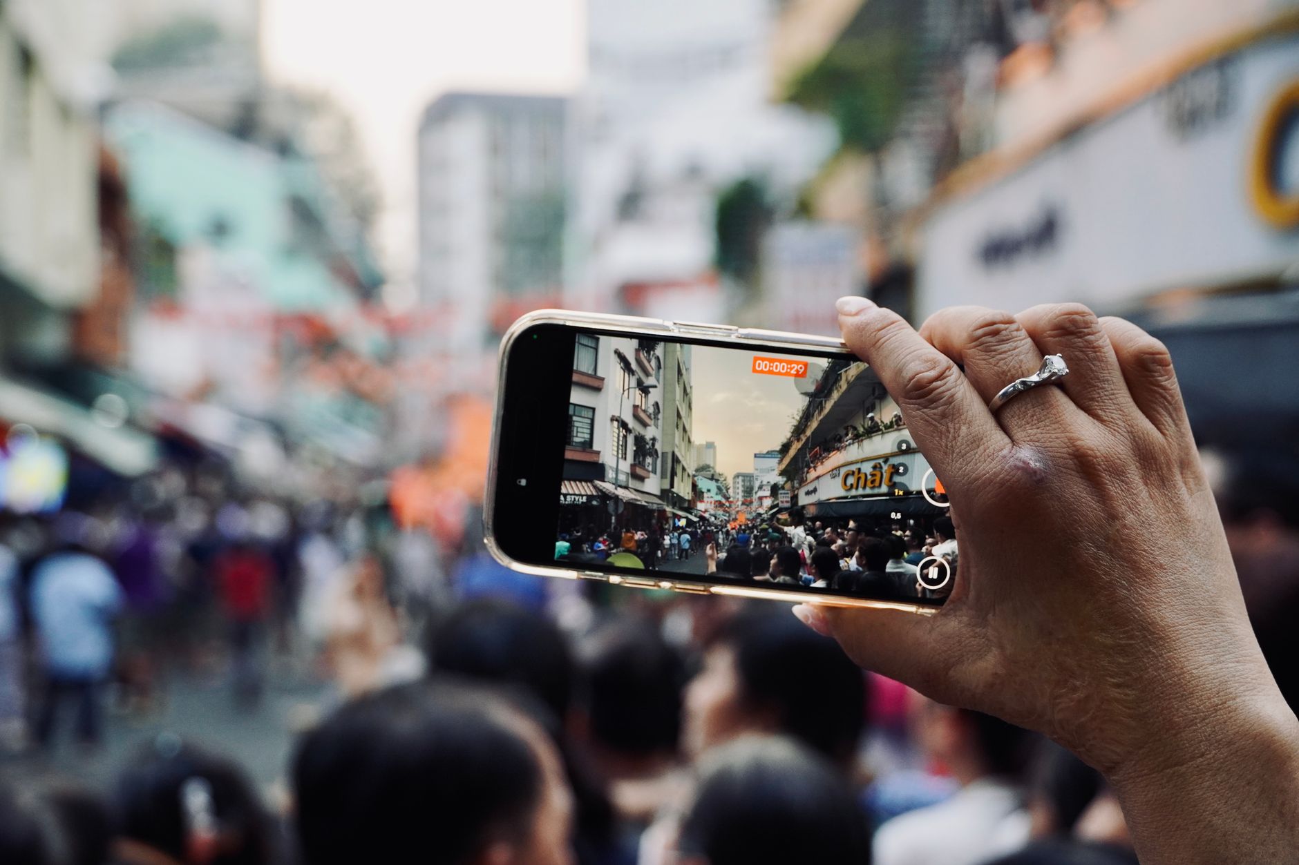 Hand holding smartphone capturing bustling city street scene with crowd.