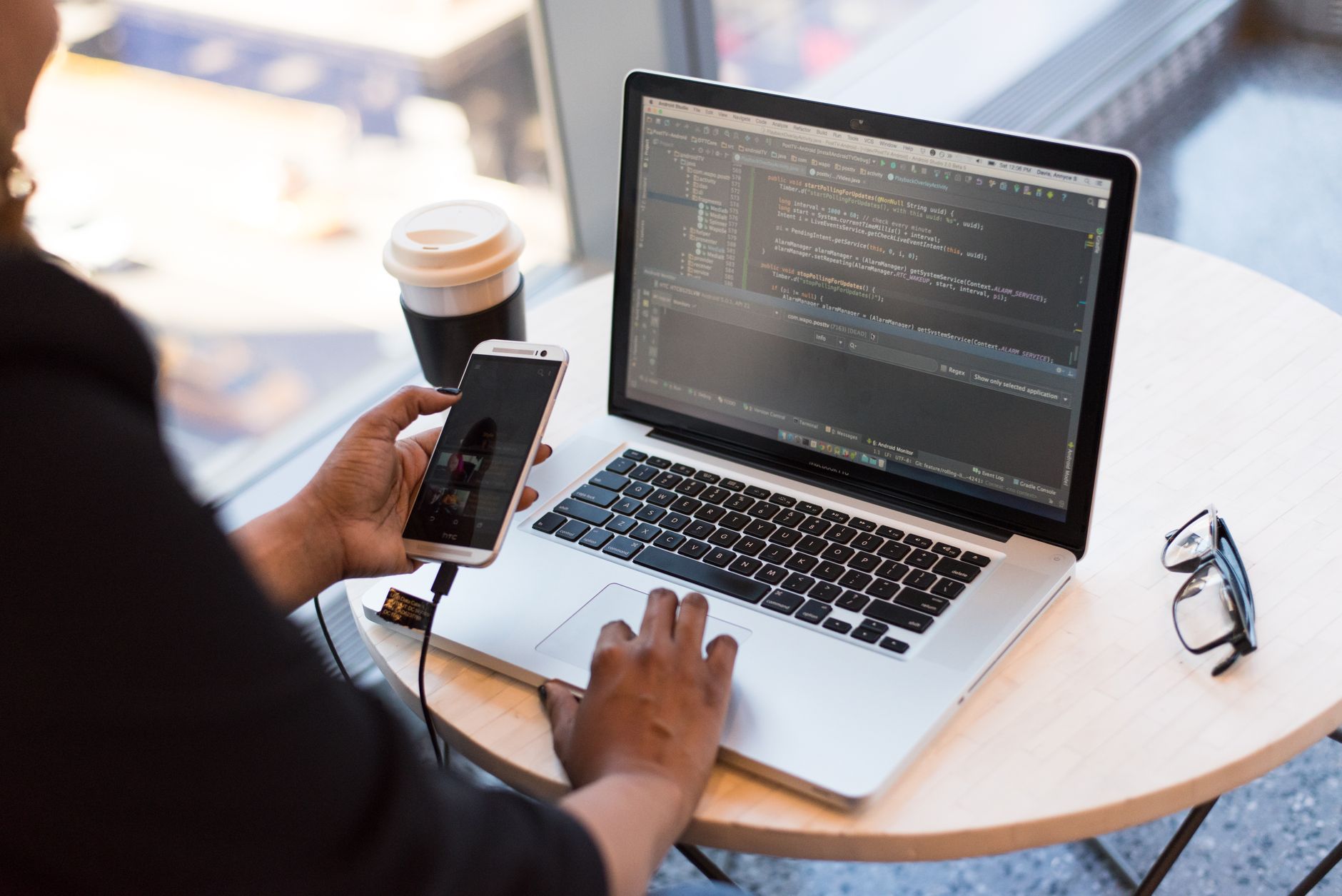 Developer working remotely, coding on a laptop with phone in hand, showcasing