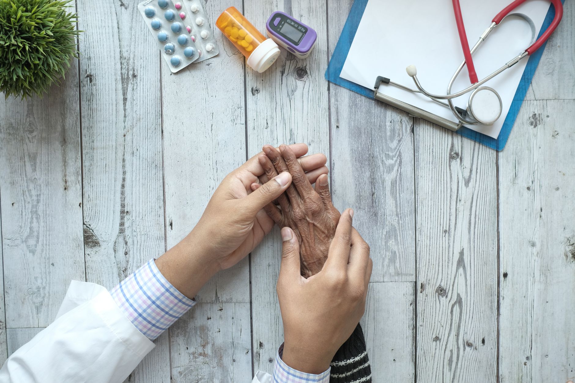 A doctor holding an elderly patient's hands on a desk with medication