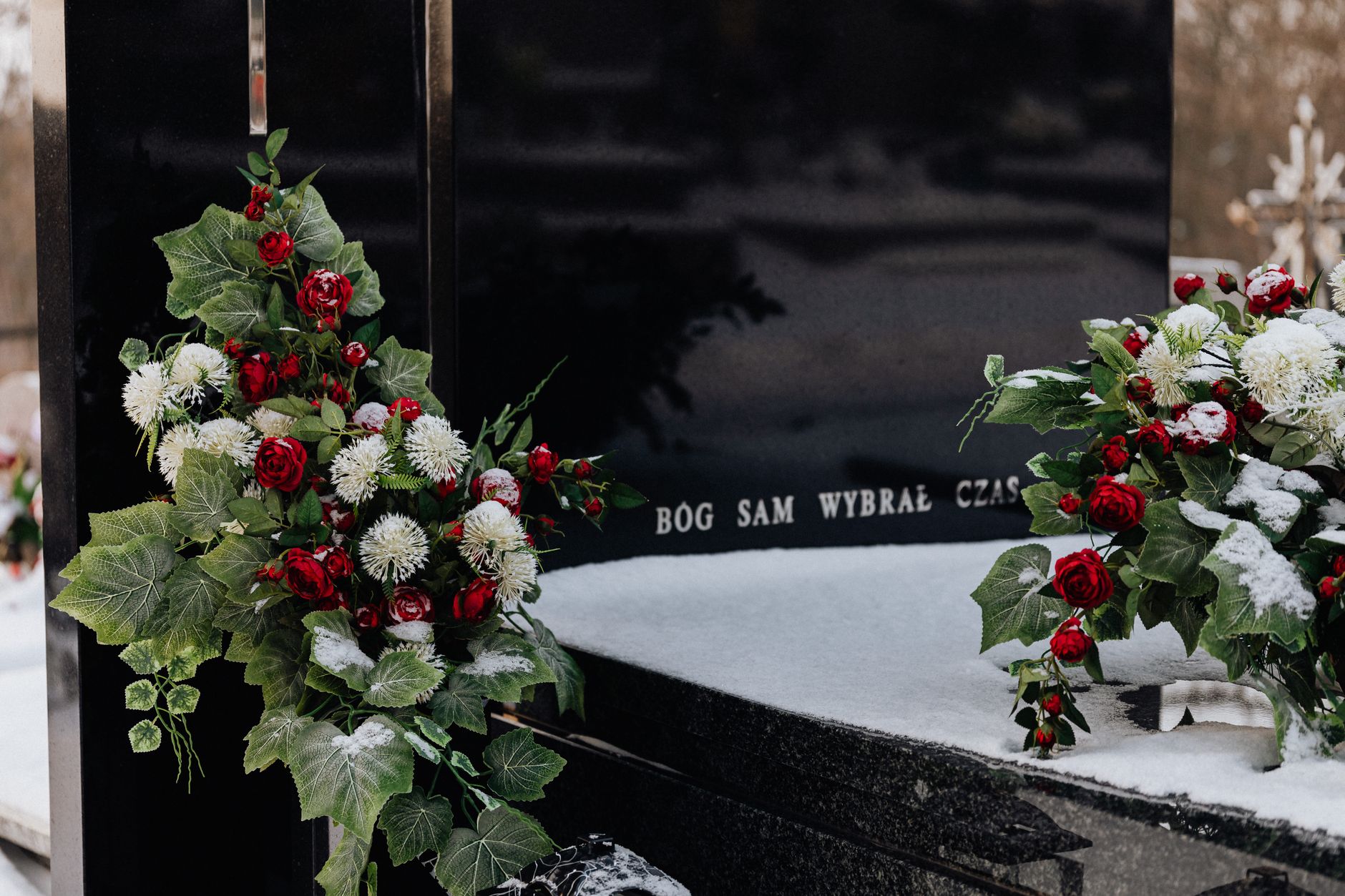 Snow-covered tombstone with red roses and white flowers, symbolizing winter's serene beauty