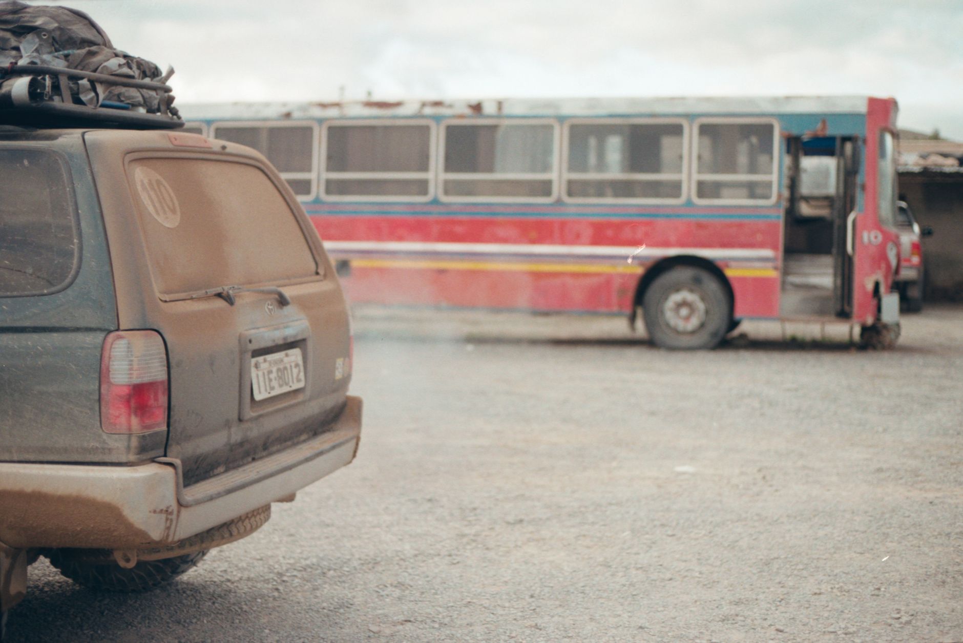 A dusty SUV and derelict bus on a gravel lot, creating a sense of neglect.