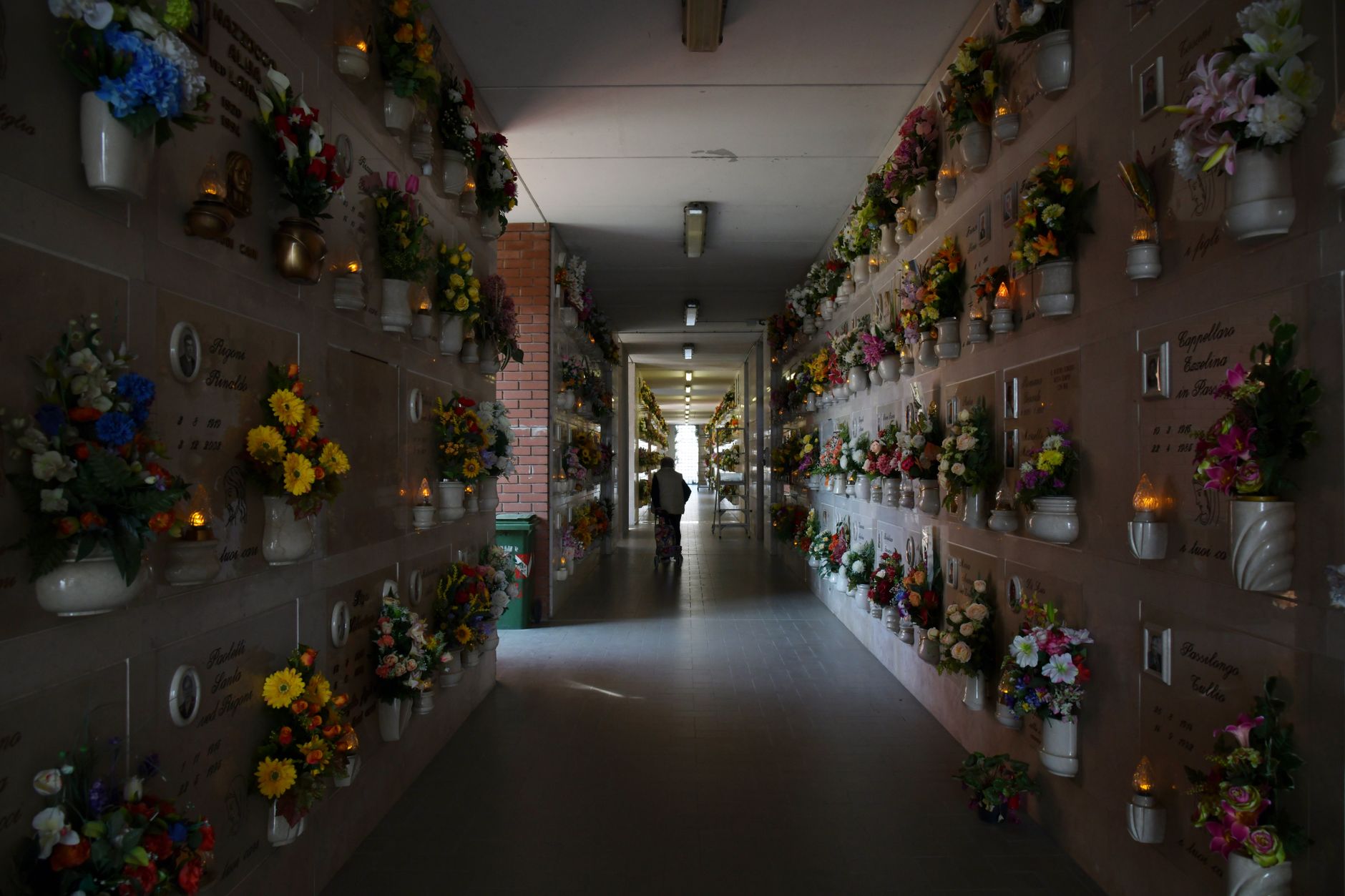 Serene columbarium corridor in Castel d'Azzano, Italy, lined with flowers and memorials.