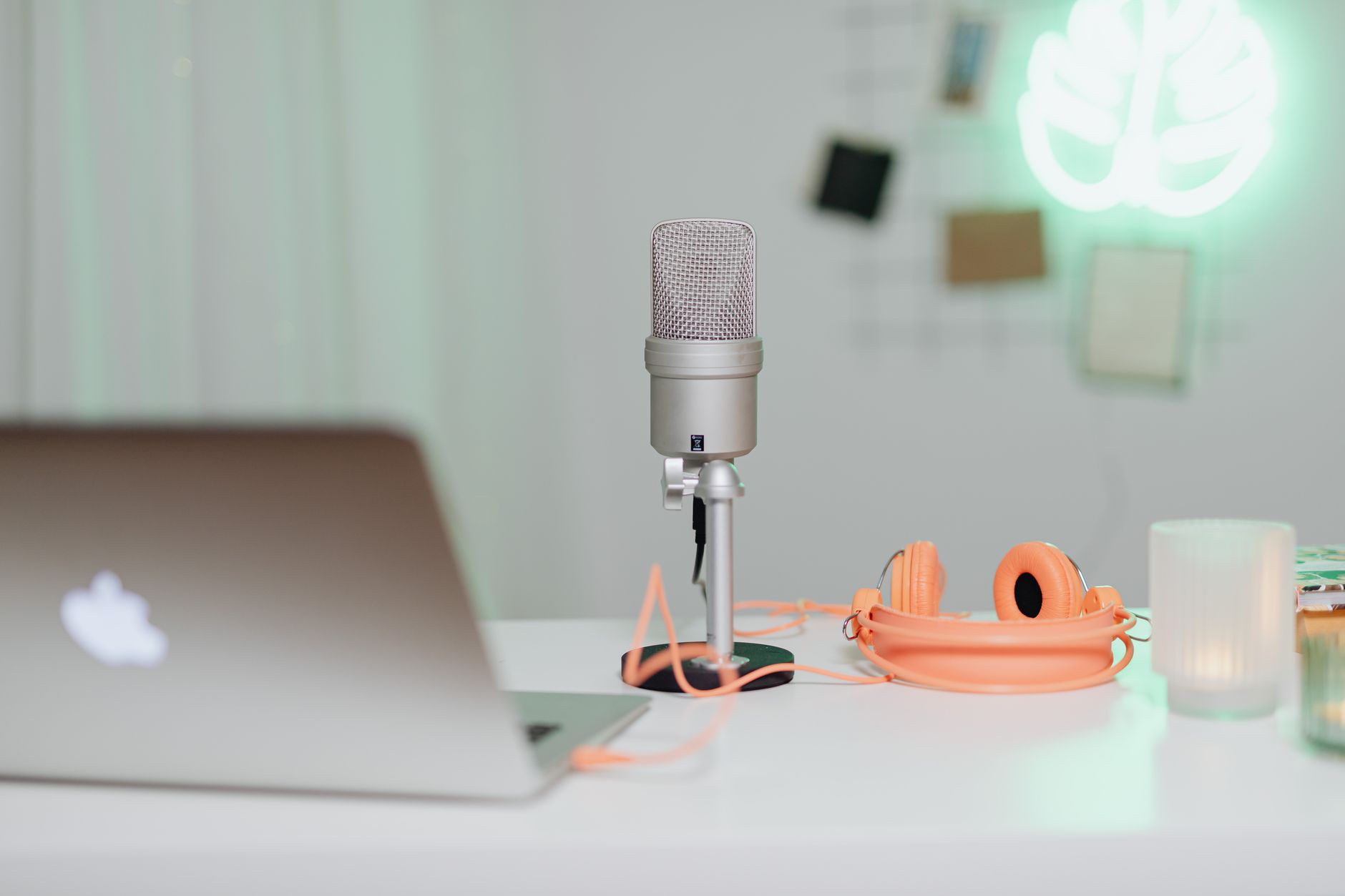 A modern desk setup featuring a condenser microphone, laptop, and headphones in