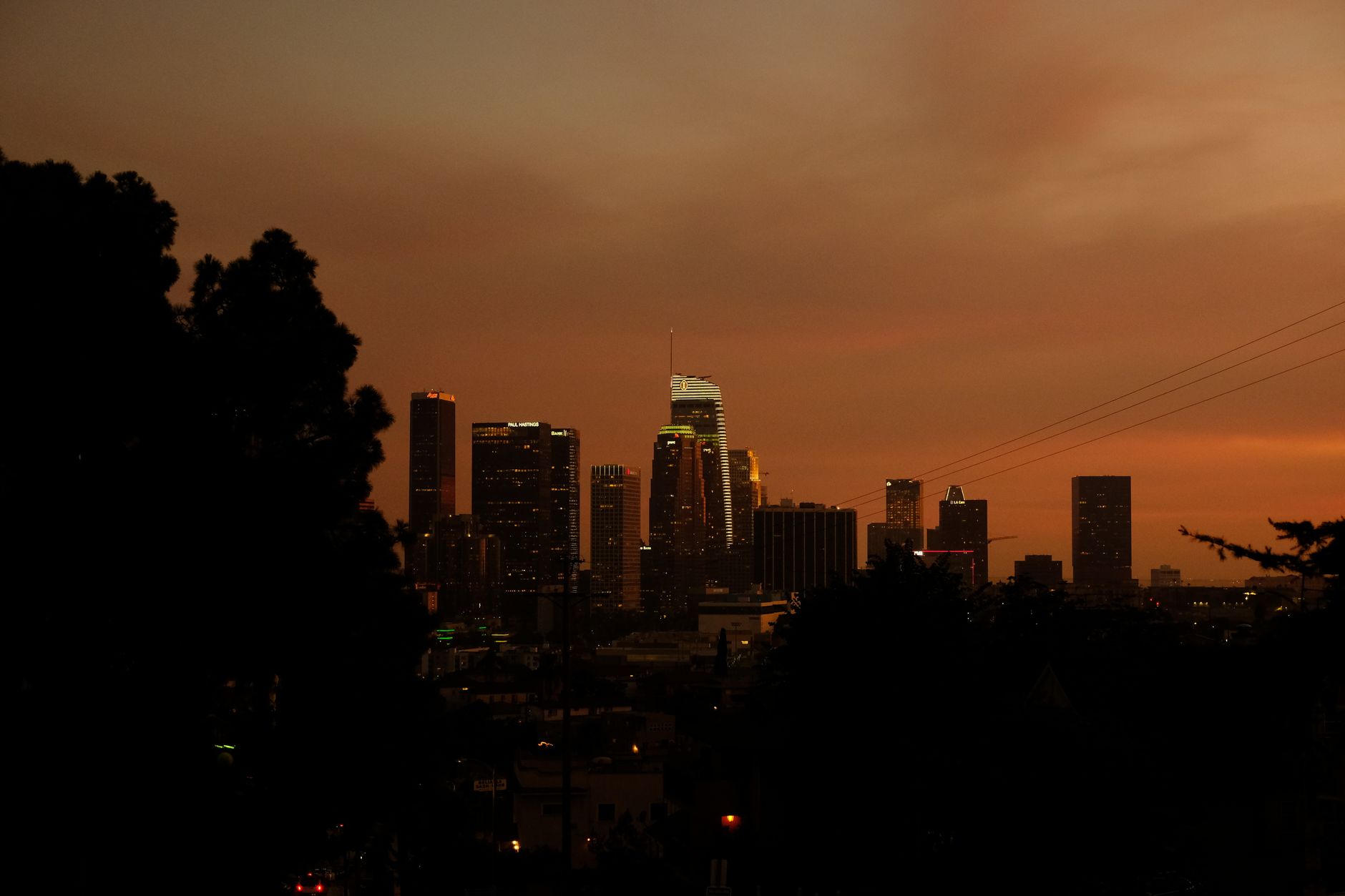 Cityscape of Los Angeles skyscrapers silhouetted against a vibrant orange sunset sky.