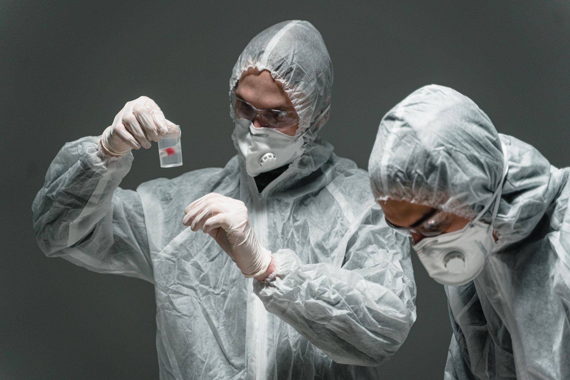 Two scientists in protective suits working in a lab, examining samples safely.