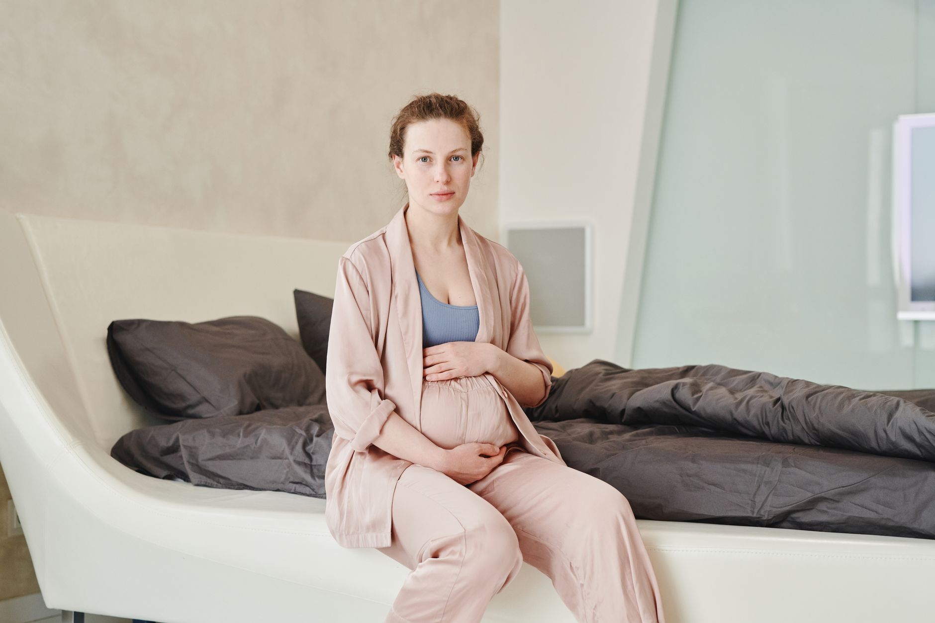 A serene image of a pregnant woman sitting on a bed, embracing