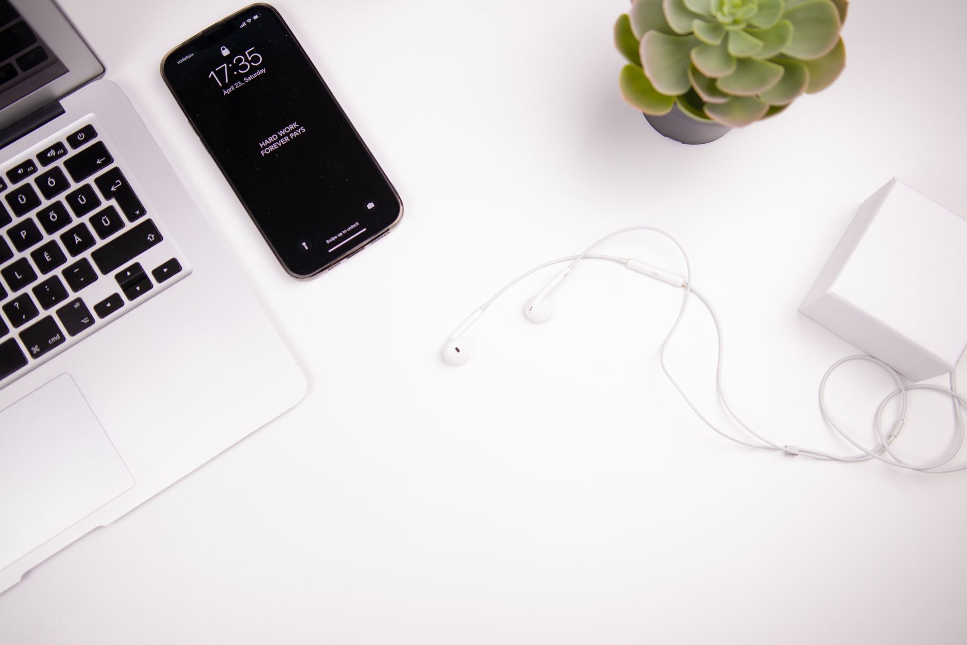 Elegant minimalist workspace featuring a laptop, smartphone, earbuds, and succulent on a