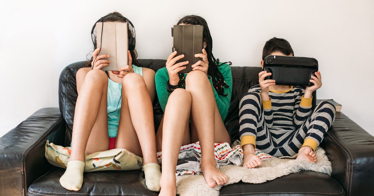 three kids with electronic devices on a sofa