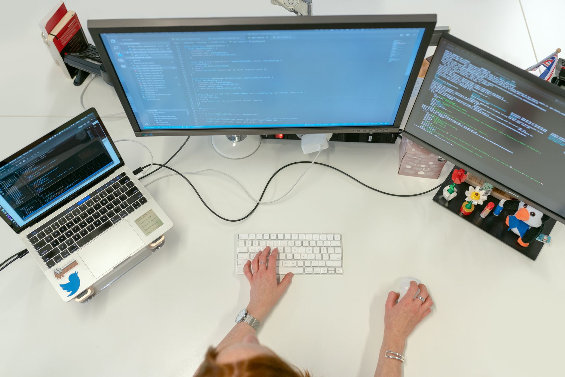 A female software engineer coding on dual monitors and a laptop in