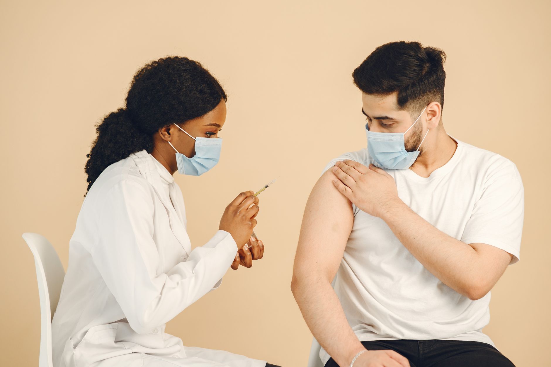 Doctor giving a vaccination to a patient wearing face masks in a