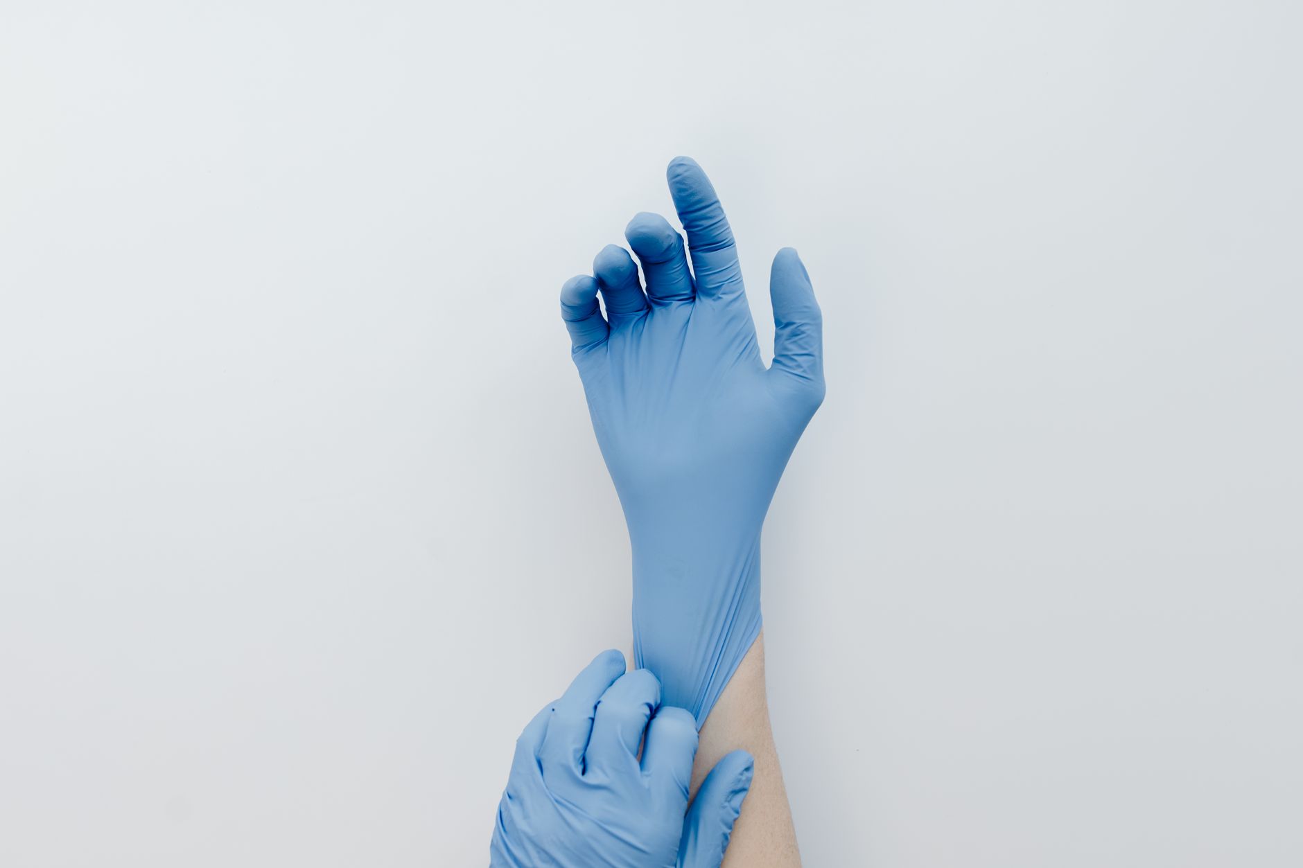 Close-up of hands putting on blue medical gloves against a white backdrop.