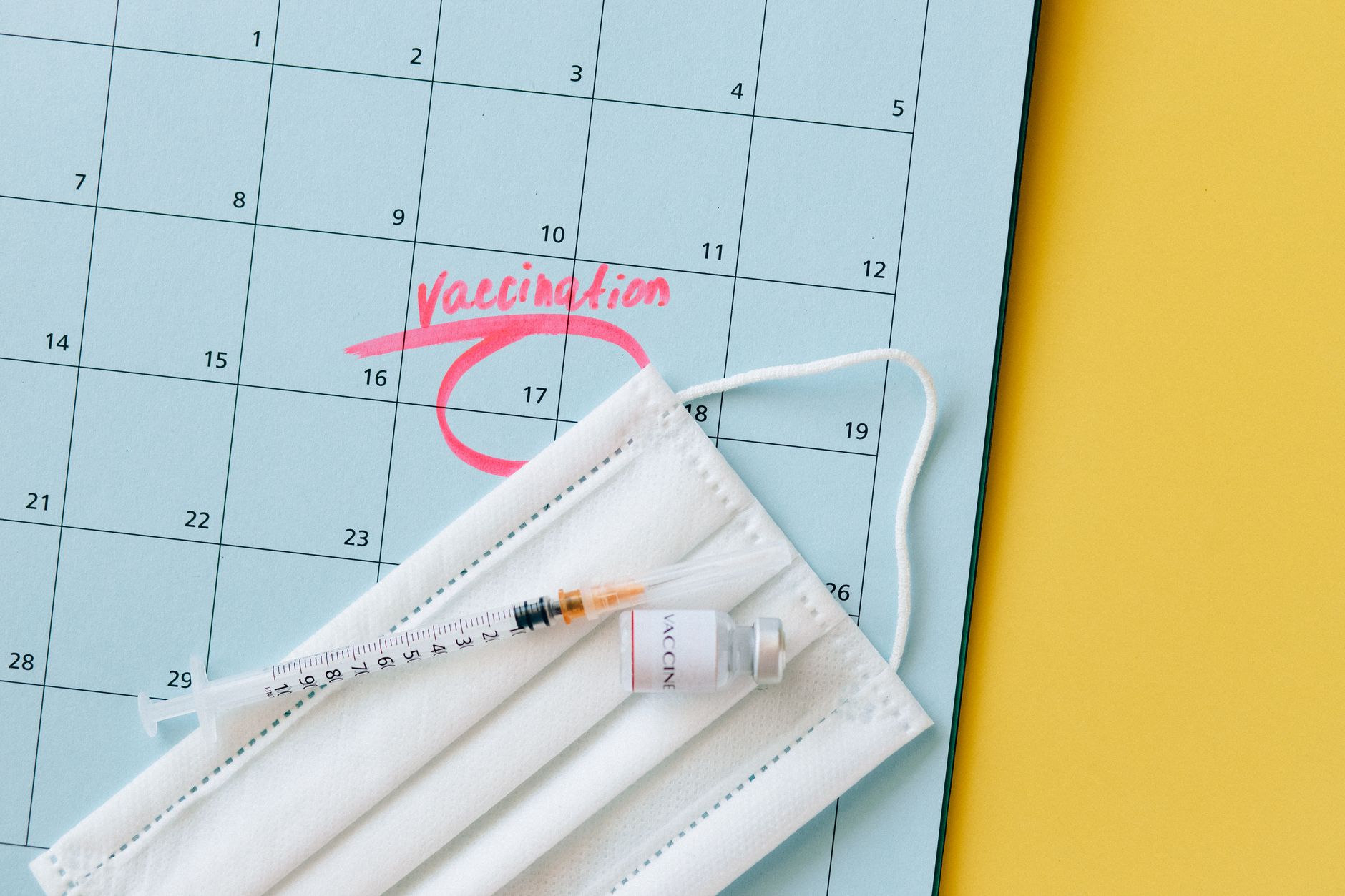 Close-up of a calendar marked for vaccination, with a syringe and face