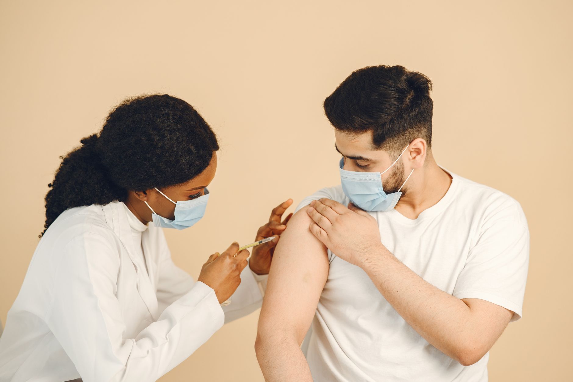 Healthcare worker in mask giving vaccination to a patient in clinical setting.
