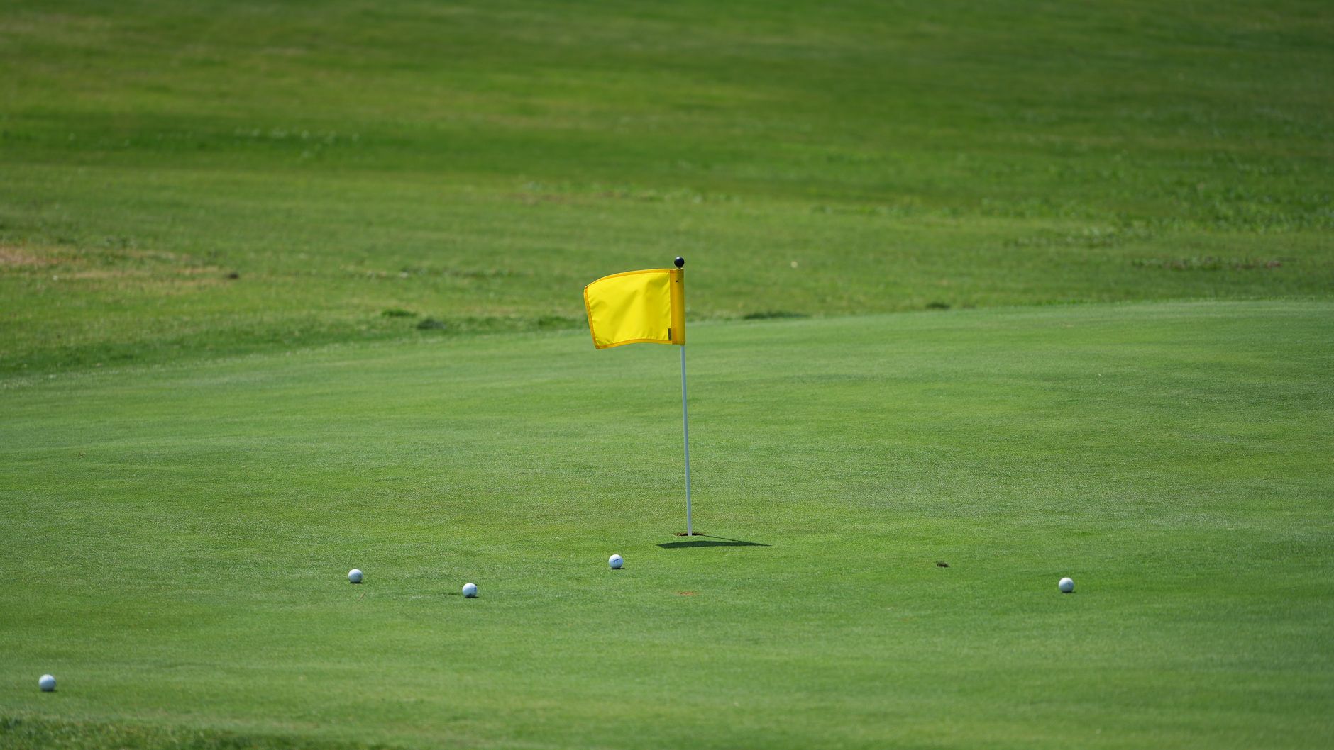 Golf course scene with yellow flag and golf balls on green under