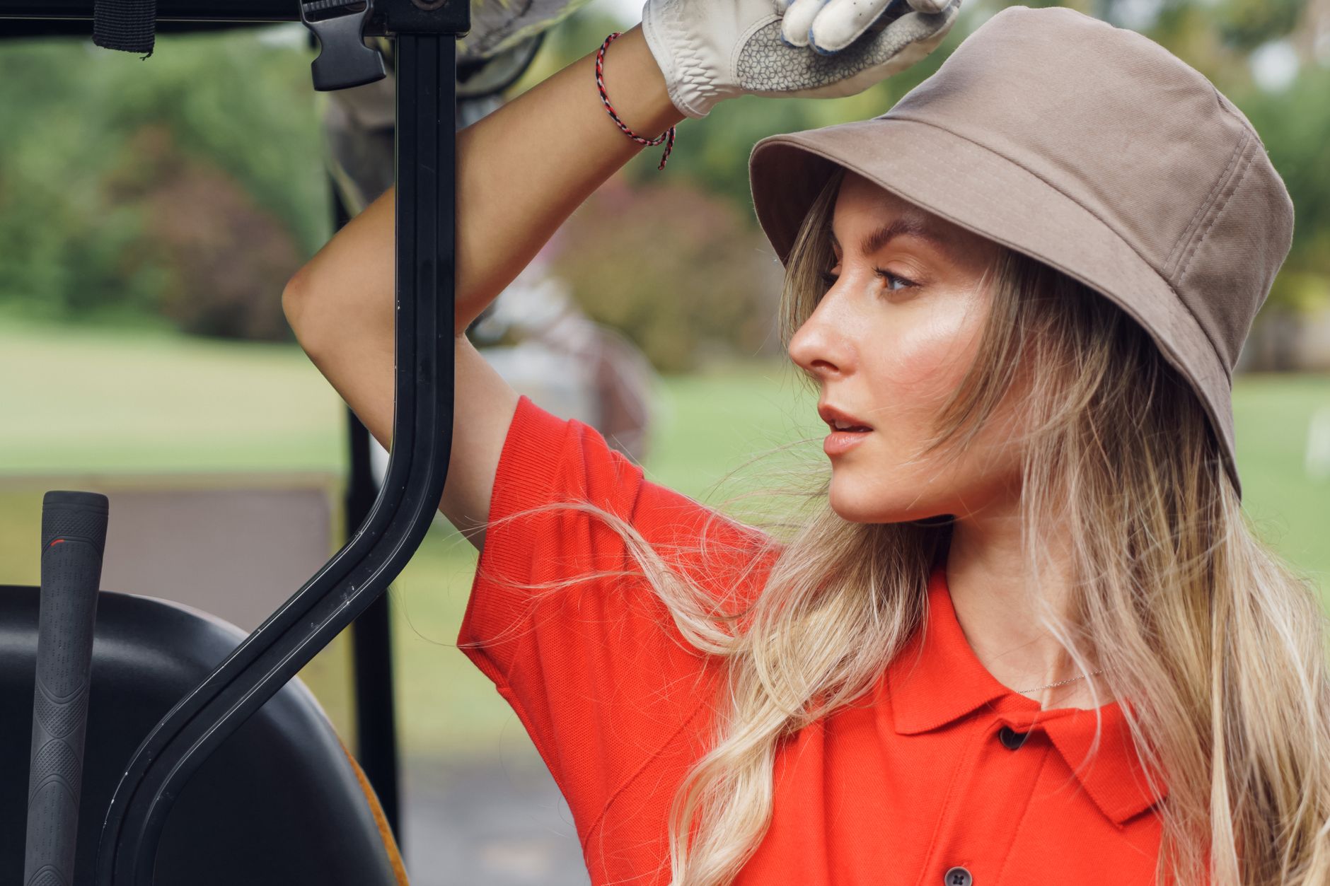 Woman golfer in red shirt with sun hat on a golf course looking thoughtful.