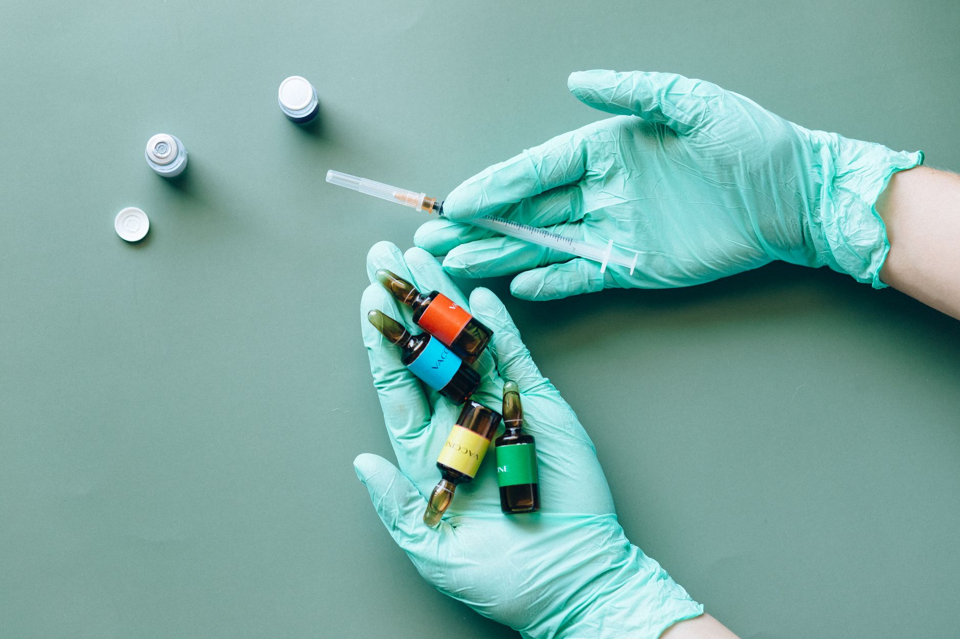 Close-up of gloved hands holding colorful medical ampules and syringe.