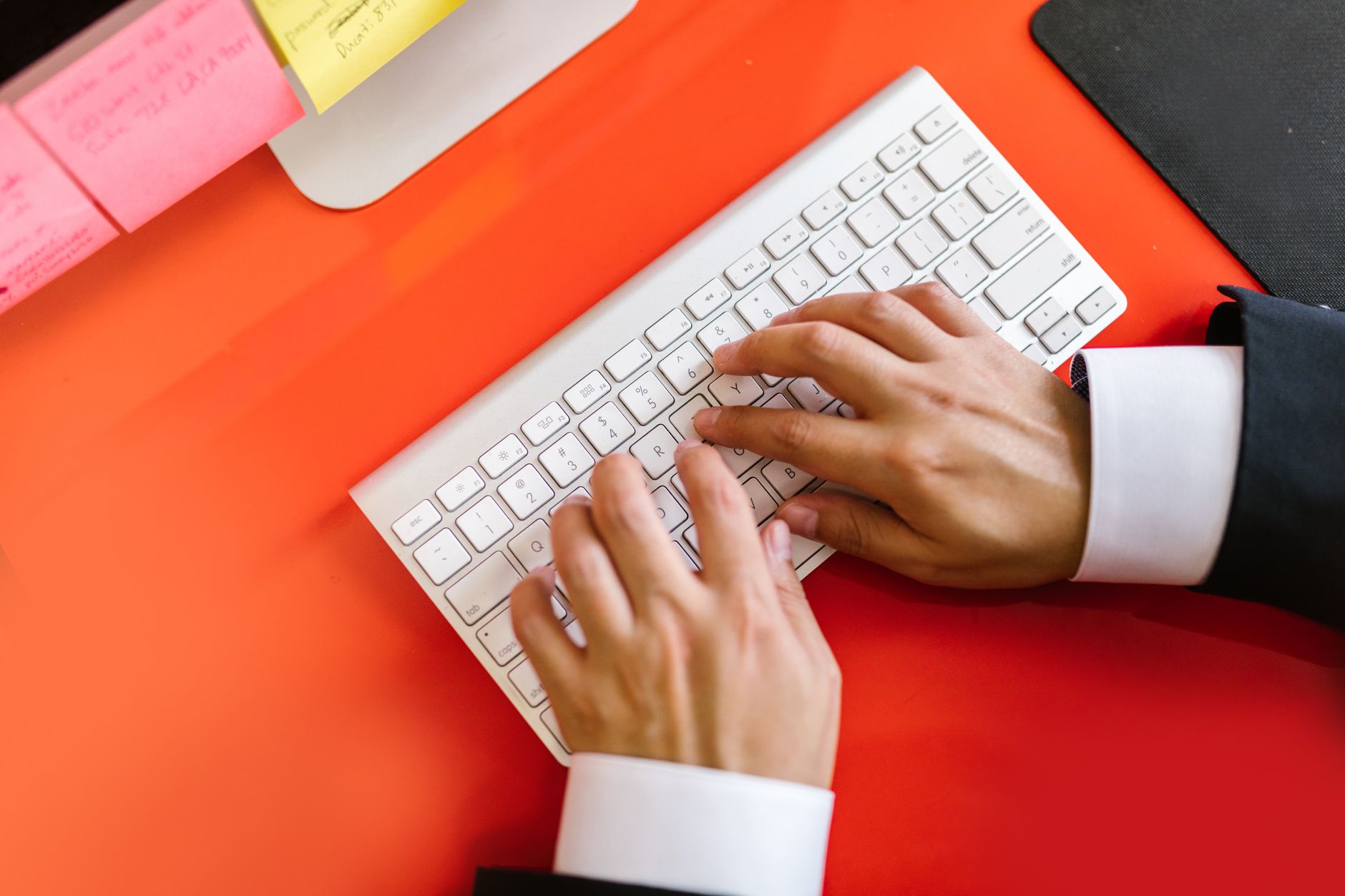 Close-up of hands typing on a wireless keyboard on an orange desk, ideal for tech and business themes.